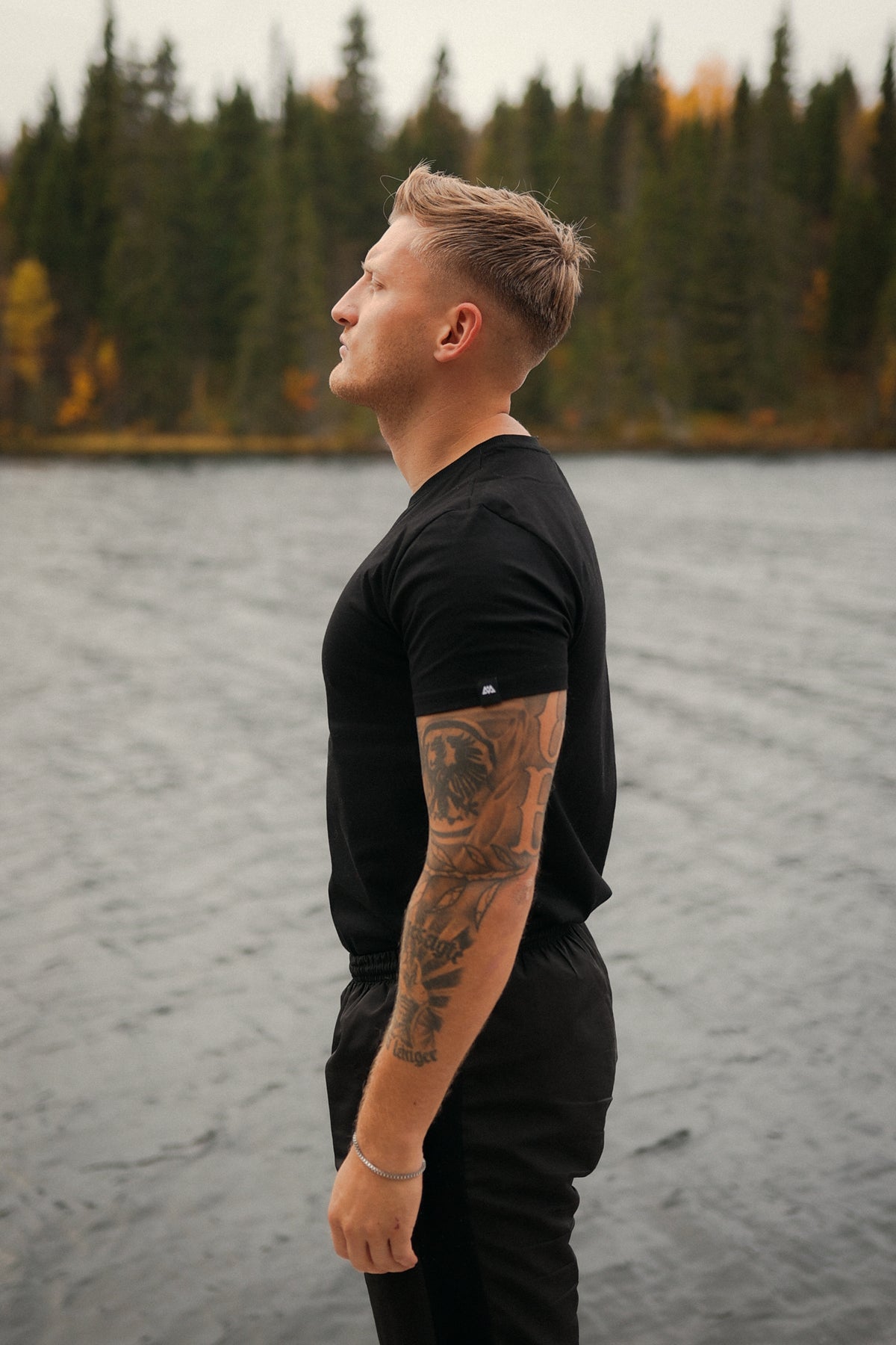 MOSAIK Black T-Shirt, white label at sleeve end, side view