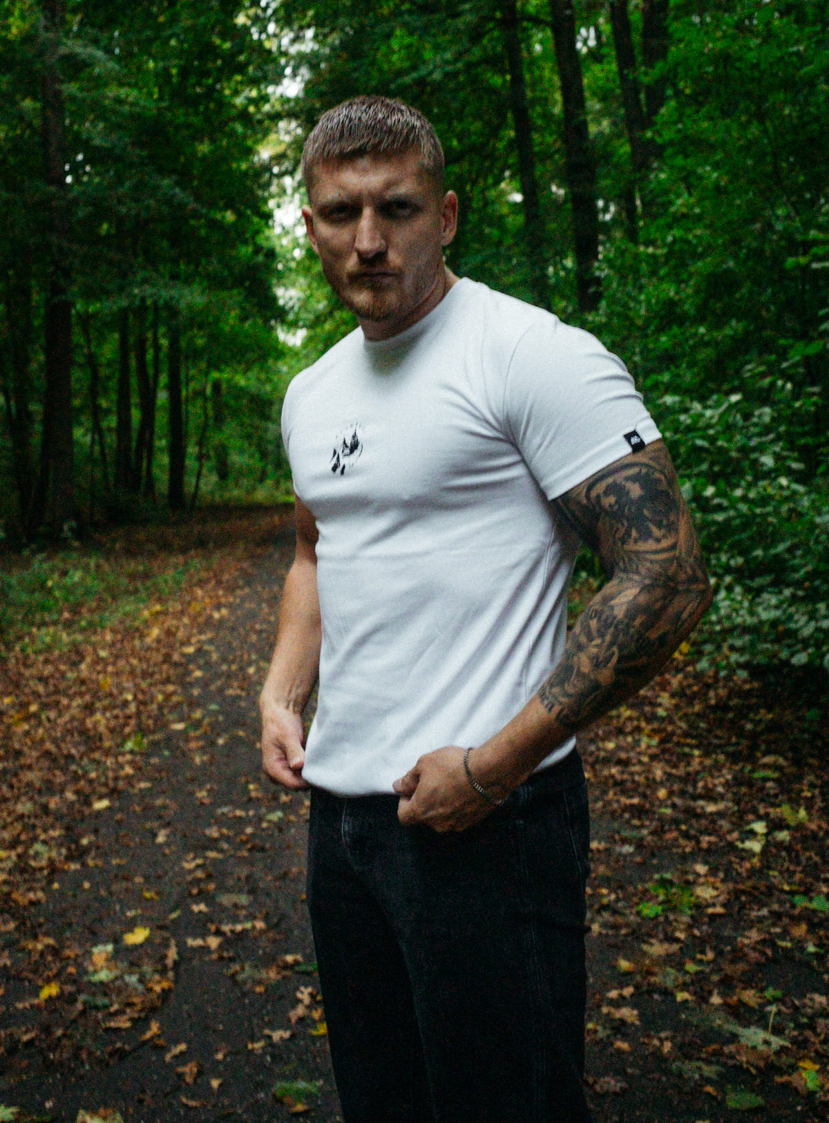 Mann trägt weißes Avantura T-Shirt mit kleinem Brustlogo im Wald