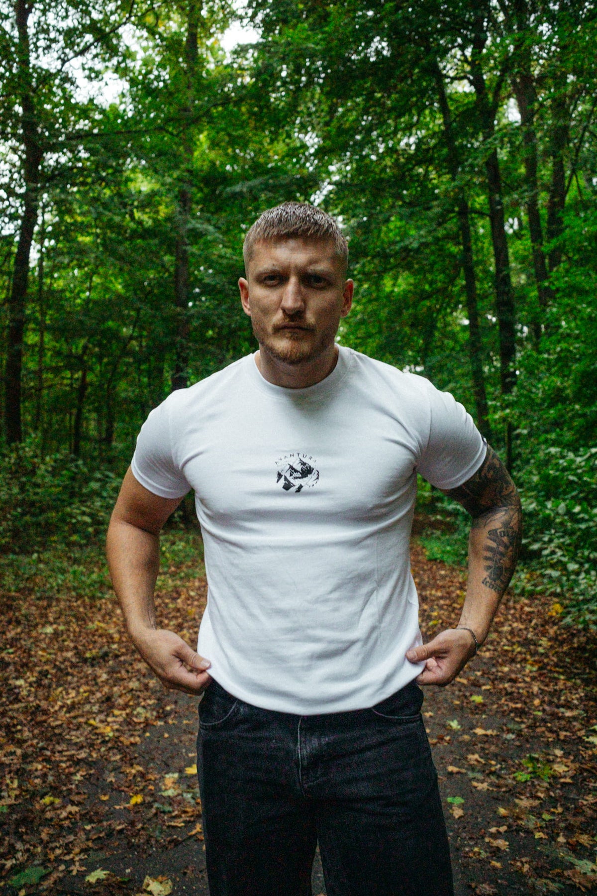 Weißes T-Shirt mit Brustlogo in Outdoor-Szene, Mann hält Stoff fest