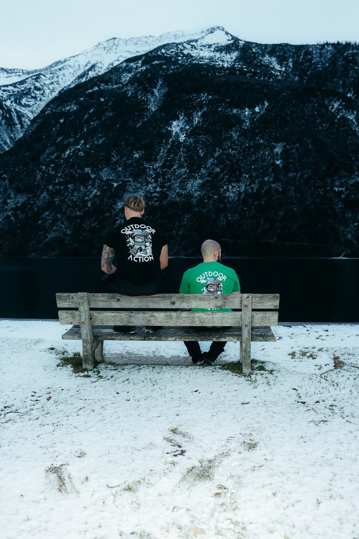 Green and black graphic print t-shirts worn by men sitting on bench in winter landscape