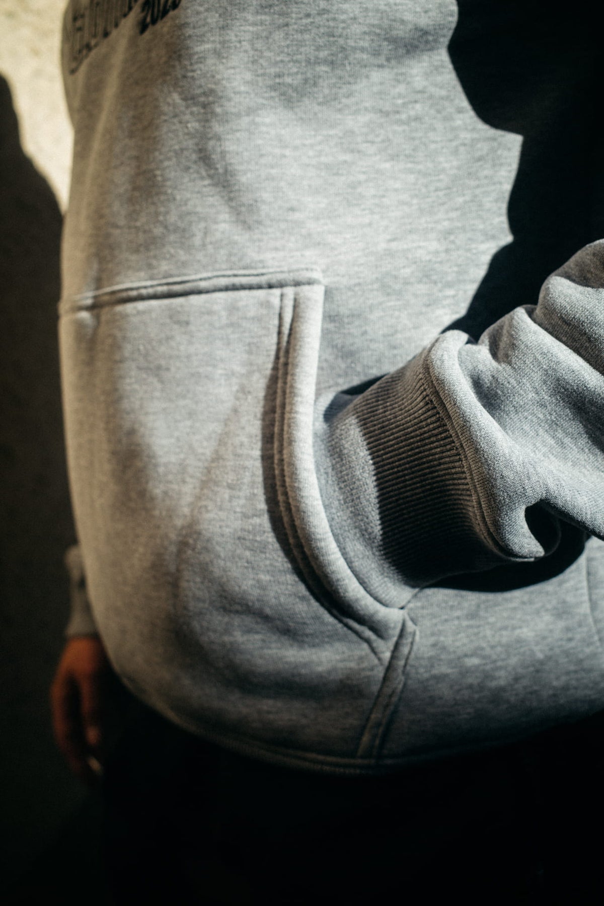 Detailansicht grauer Hoodie: seitliche Tasche und geripptes Ärmelbündchen