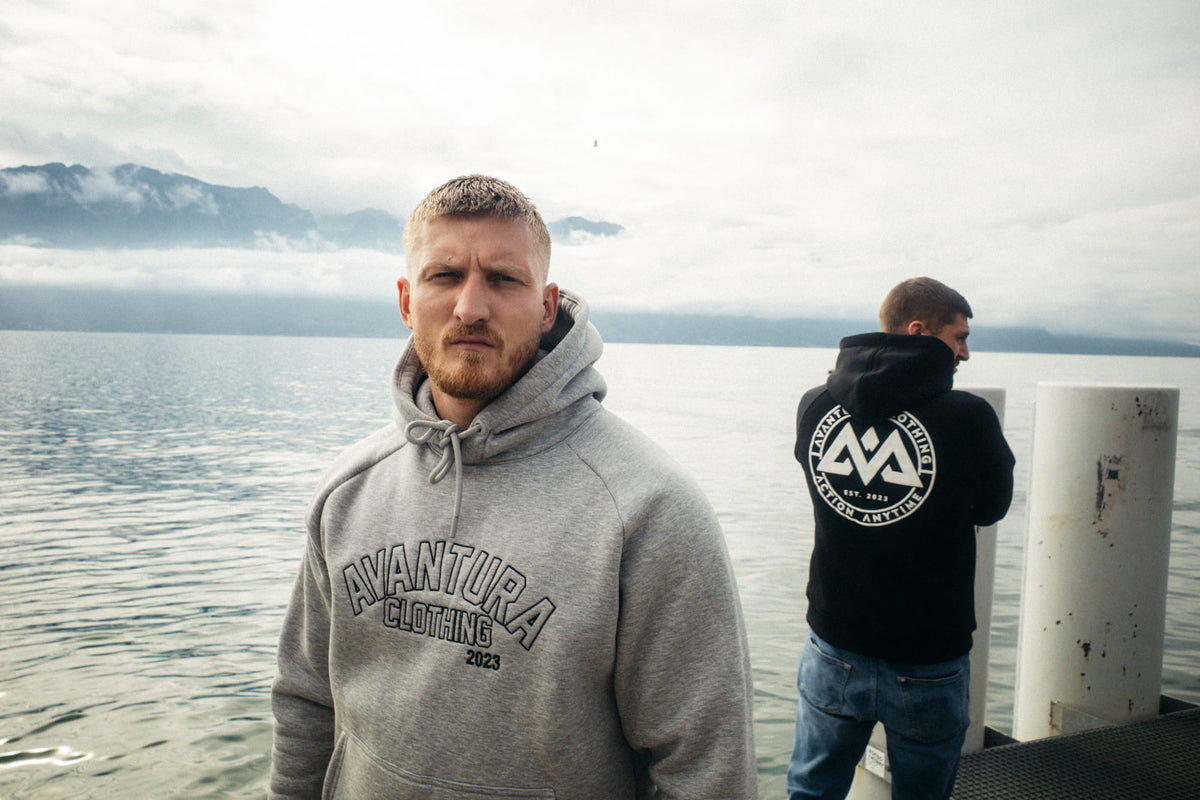 Grauer Avantura Outline Hoodie mit gesticktem Logo, getragen im Outdoor-Stil