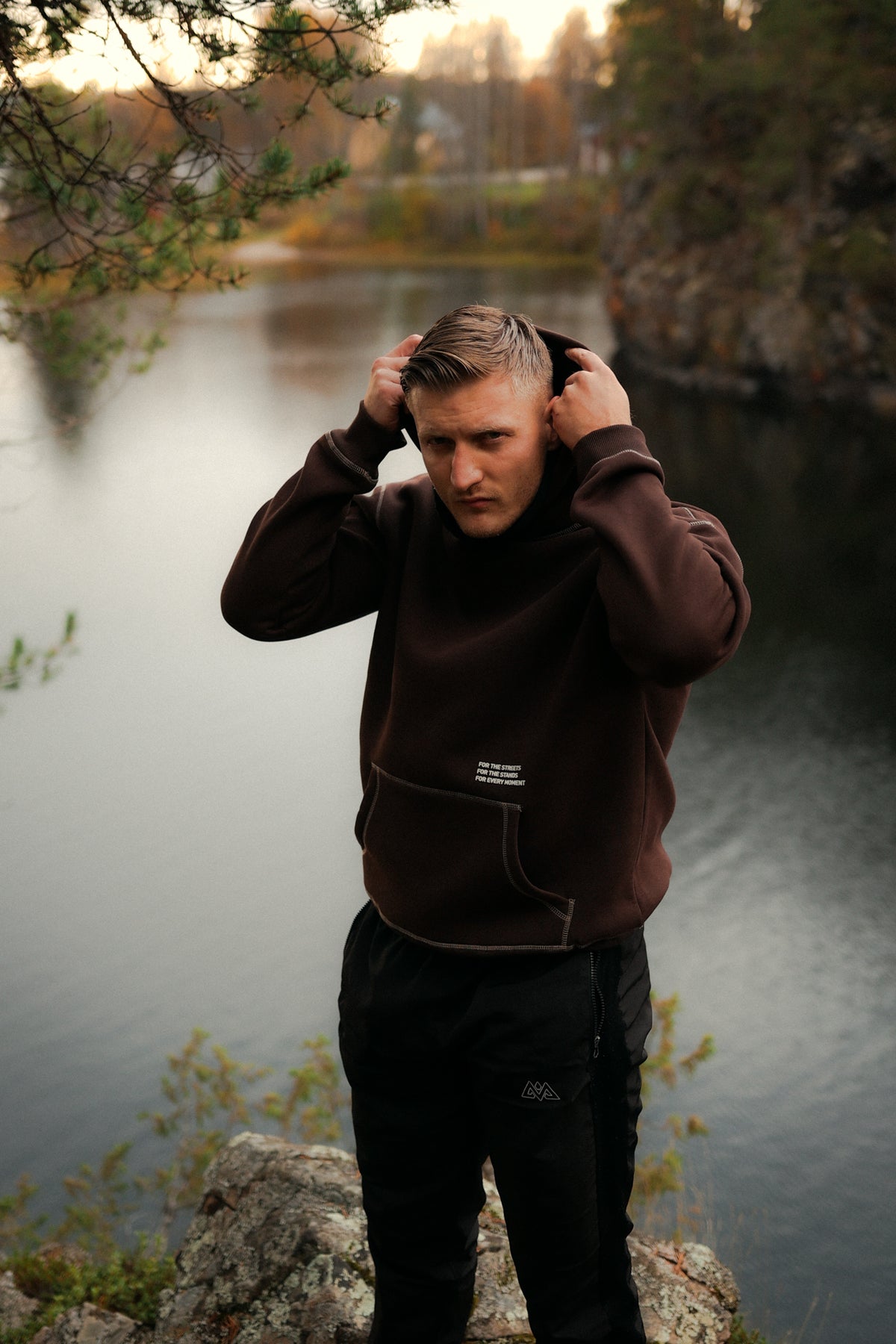 Man adjusting hood of brown hoodie with kangaroo pocket and print