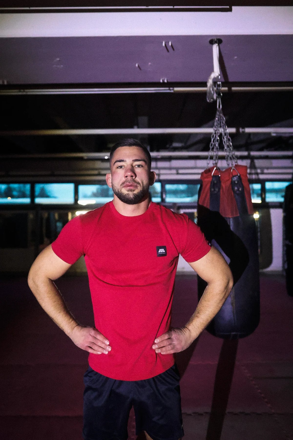 Model wearing red crew-neck t-shirt with logo patch