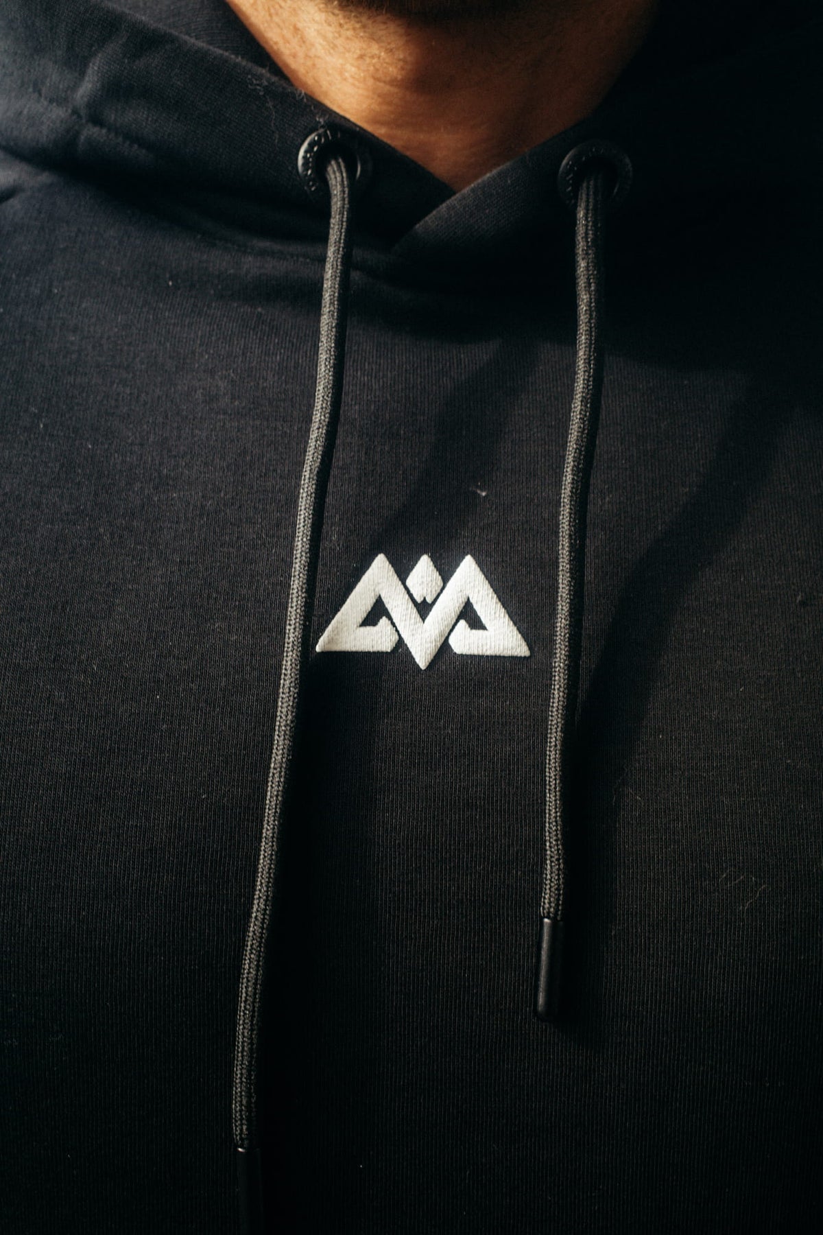 Detail schwarzer Hoodie gesticktes geometrisches Logo und Kordelzug