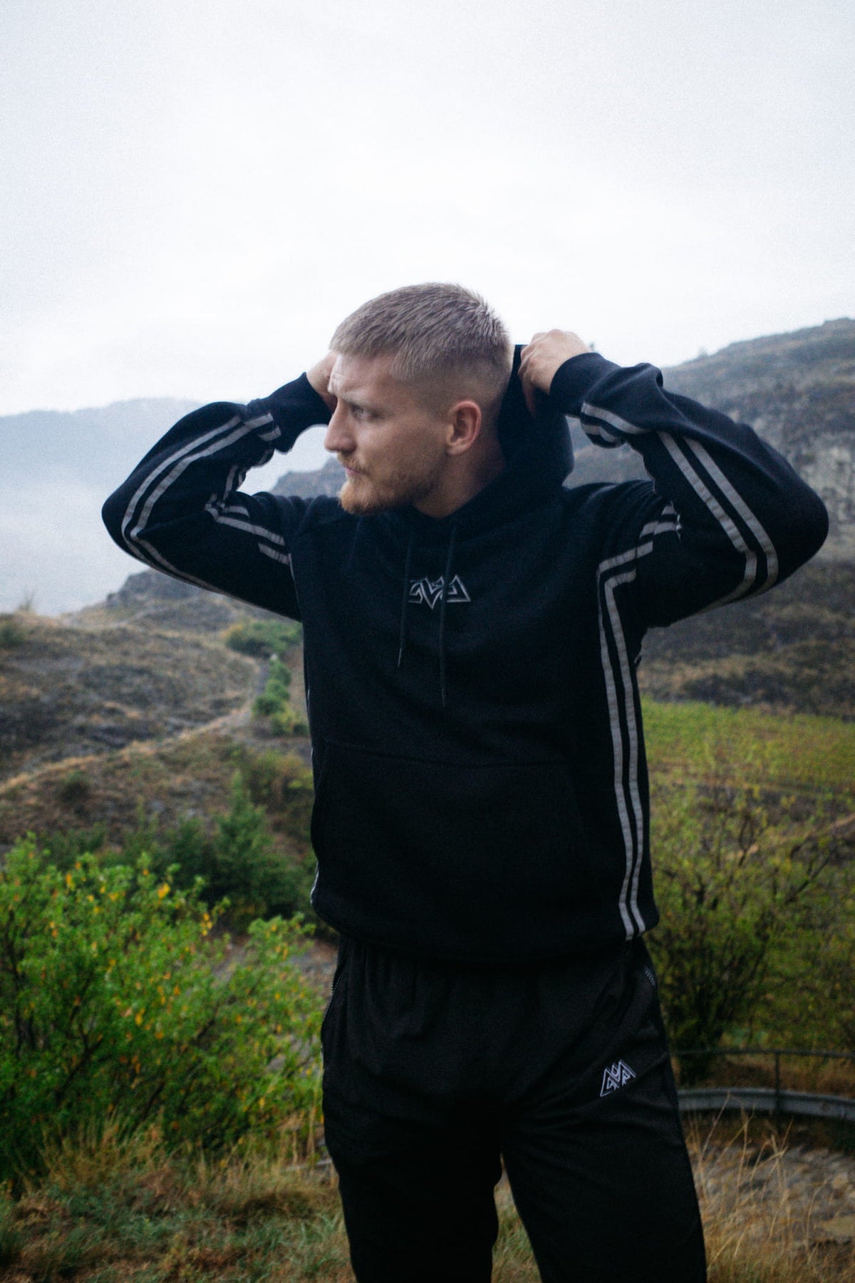 Man pulls hood of black reflective hoodie in mountain landscape