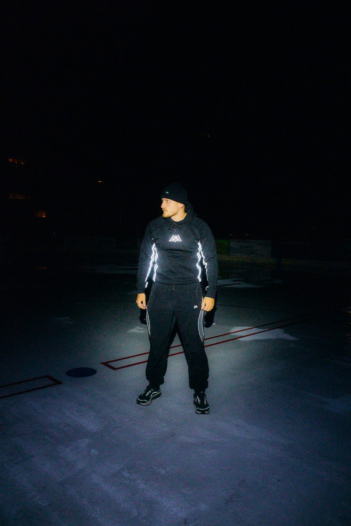 Reflective hoodie with geometric chest logo and side stripes at night