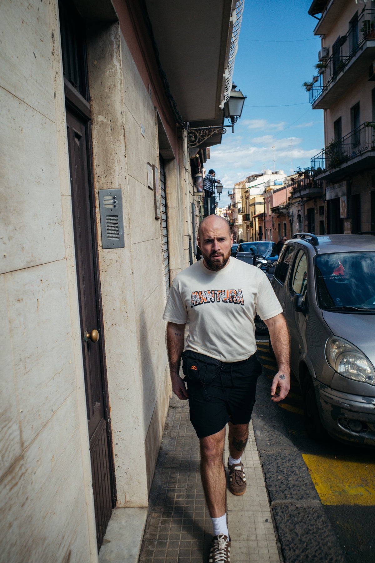 Oversized T-Shirt in Sand mit Schriftzug, getragen von Mann in Gasse
