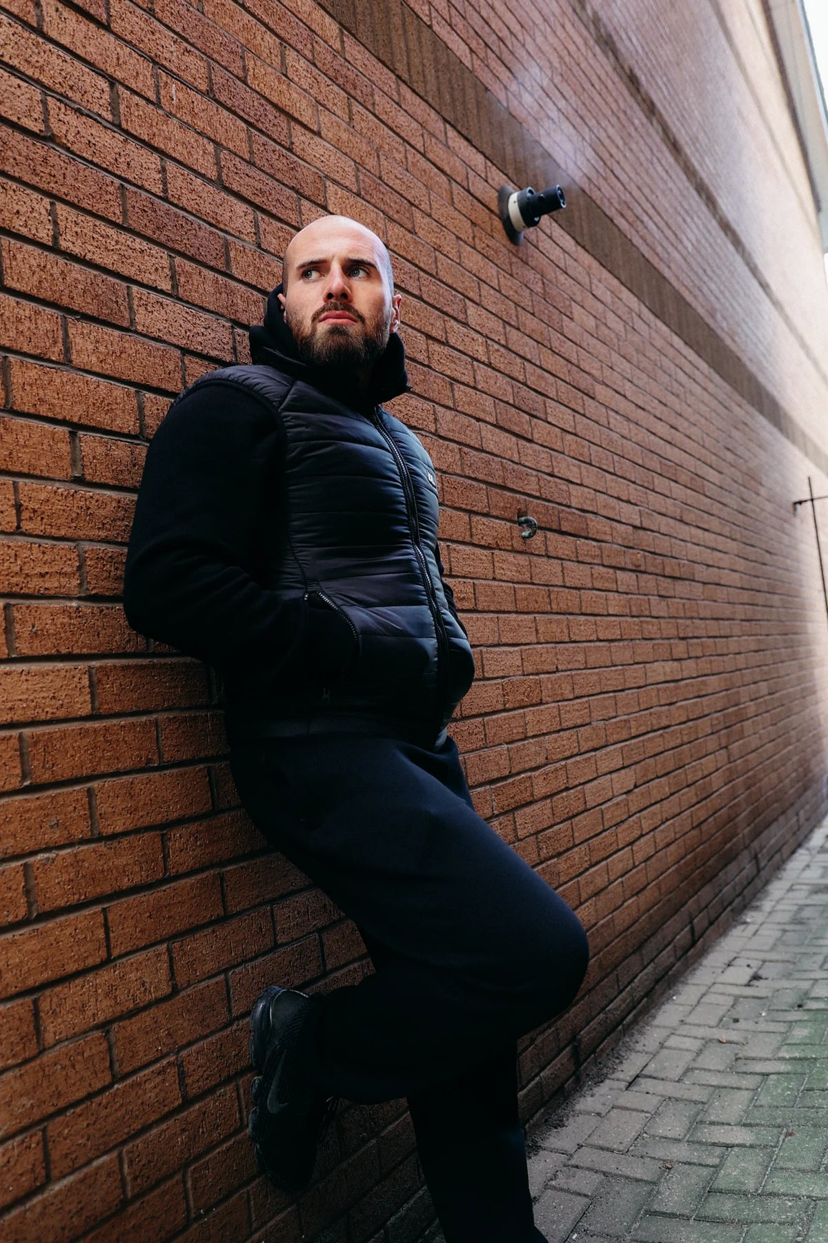 Black down vest with quilting and logo on man against red brick wall