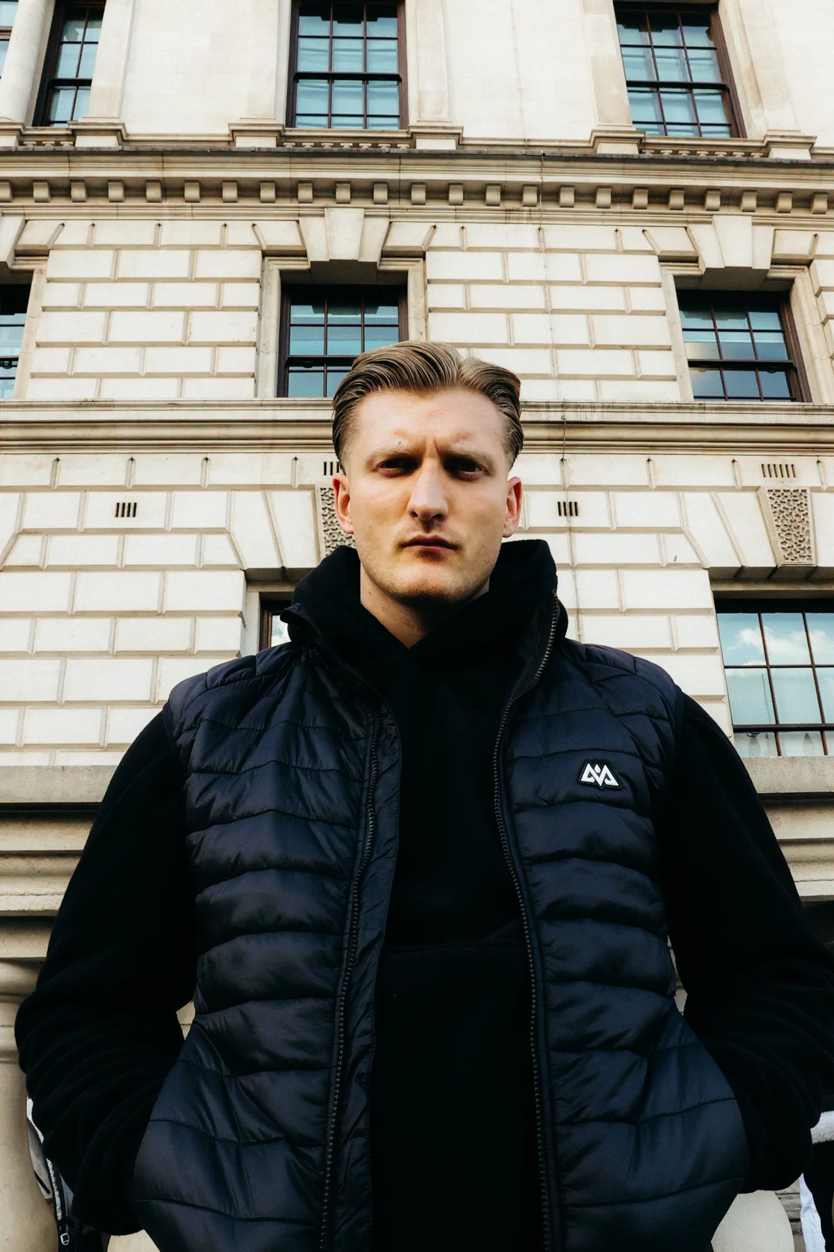 Quilted down vest with white chest logo over hoodie in front of stone house