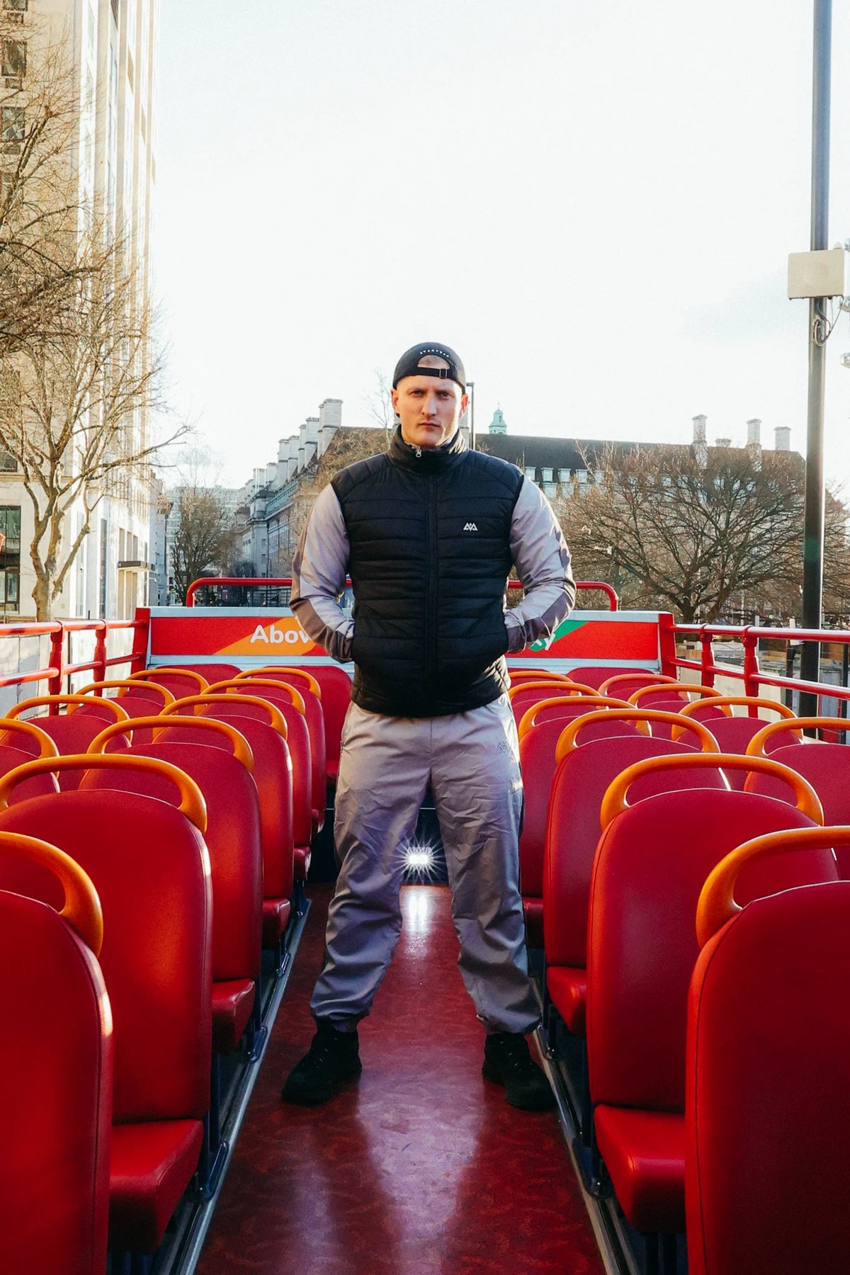 Black down vest with logo on bus upper deck over grey shirt