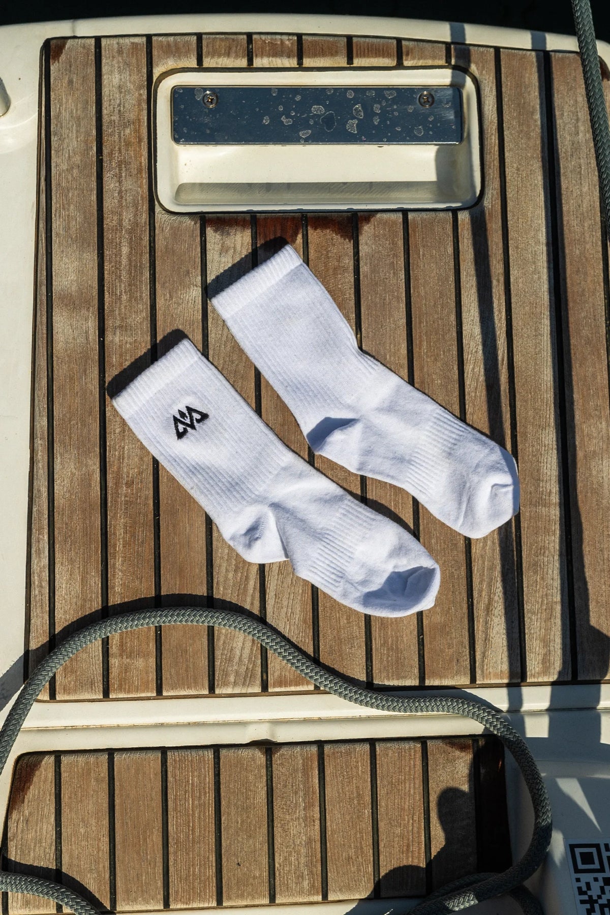 Two white crew socks with black logo flat lay on wooden deck