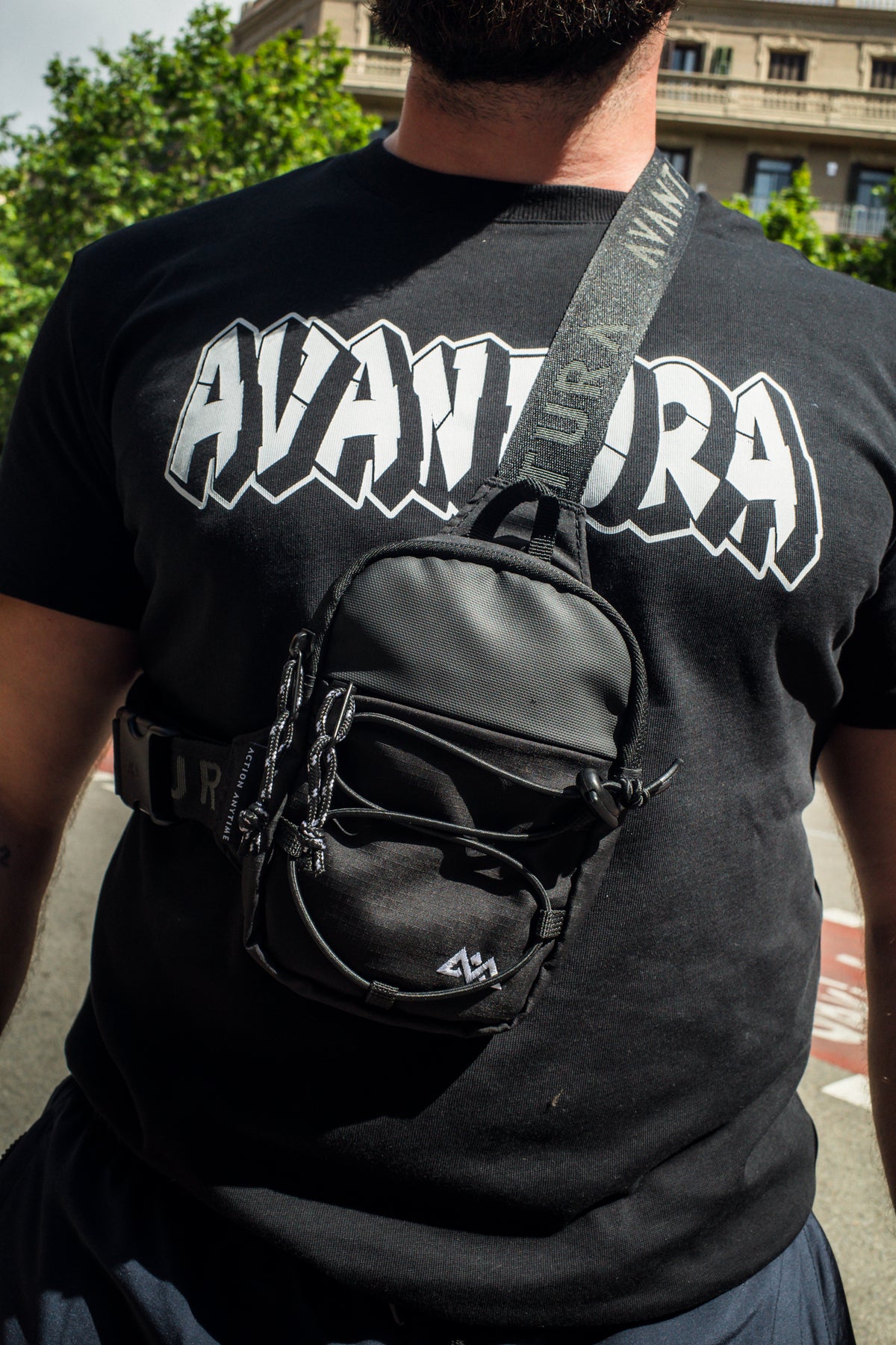 Close-up of black T-shirt with white AVANTURA logo and crossbody bag detail