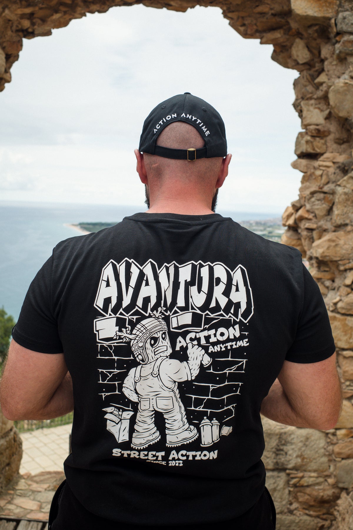 Man wearing black Avantura T-shirt with large back graphic in urban setting
