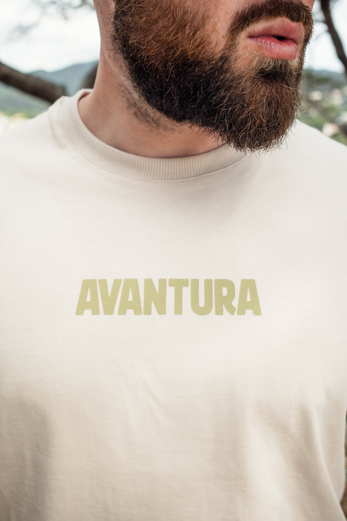Close-up of ribbed collar and olive green Avantura chest print on cream tee