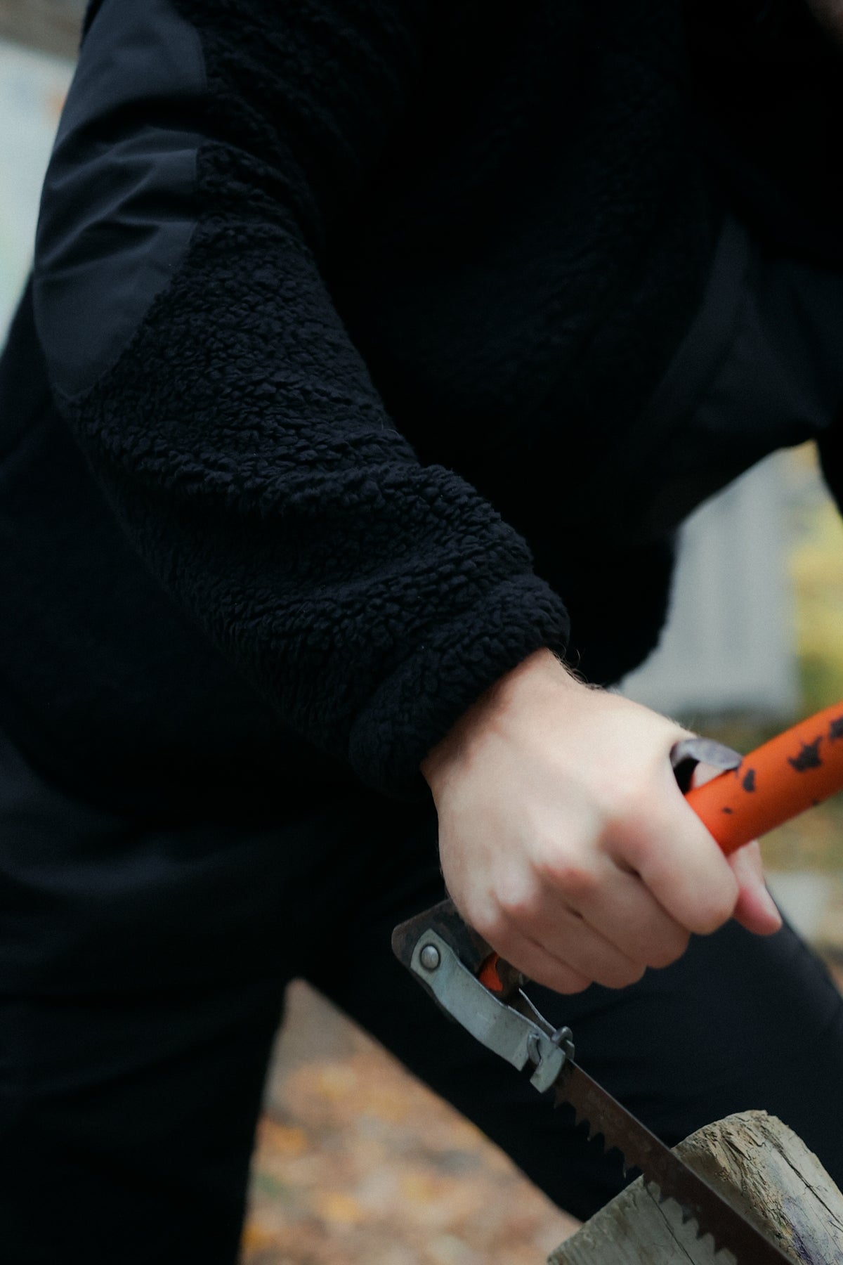 Black fleece jacket sleeve detail while using hand saw for outdoor work