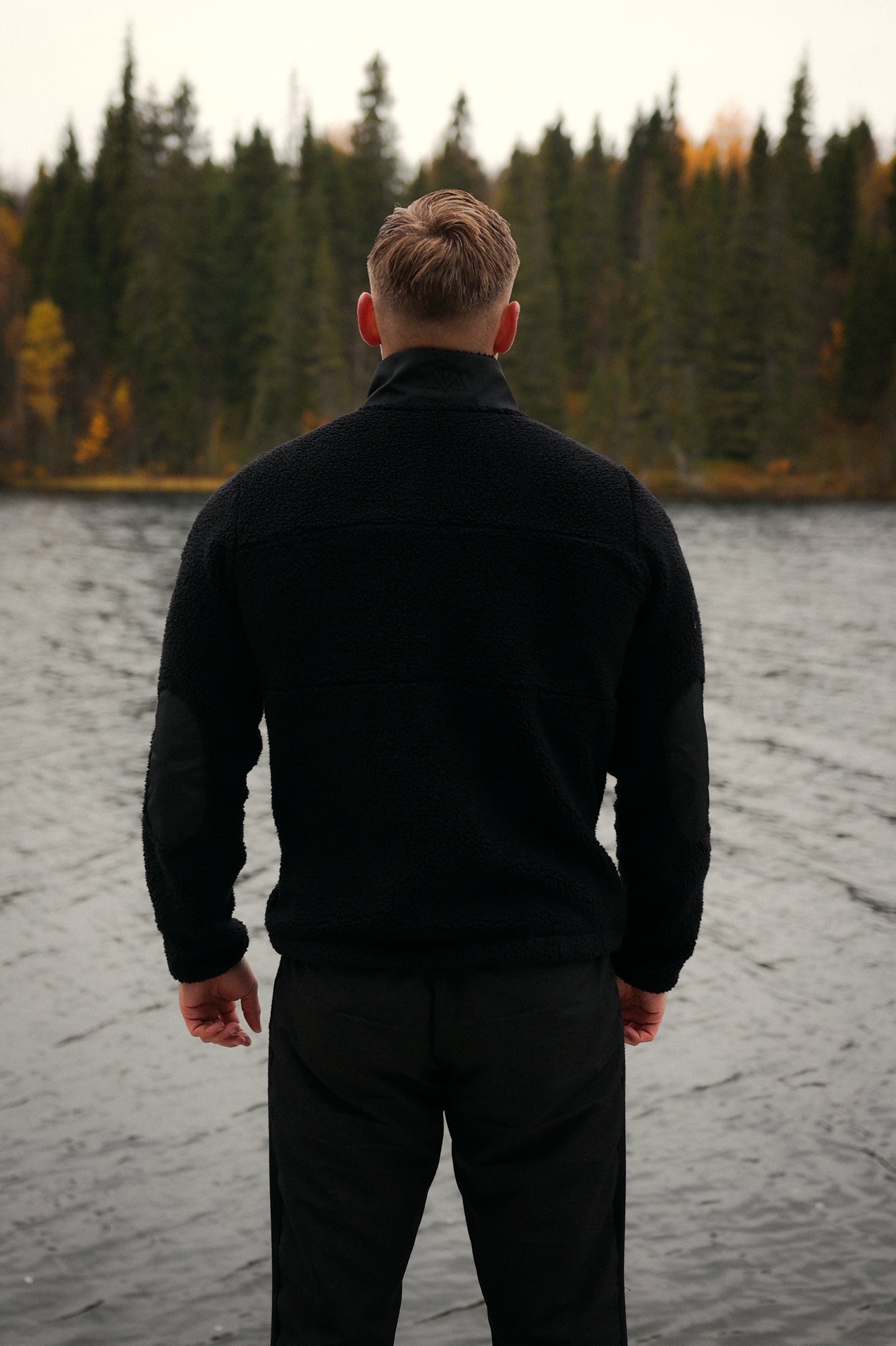 Black teddy fleece jacket with smooth shoulder panels and elbow patches worn outdoors