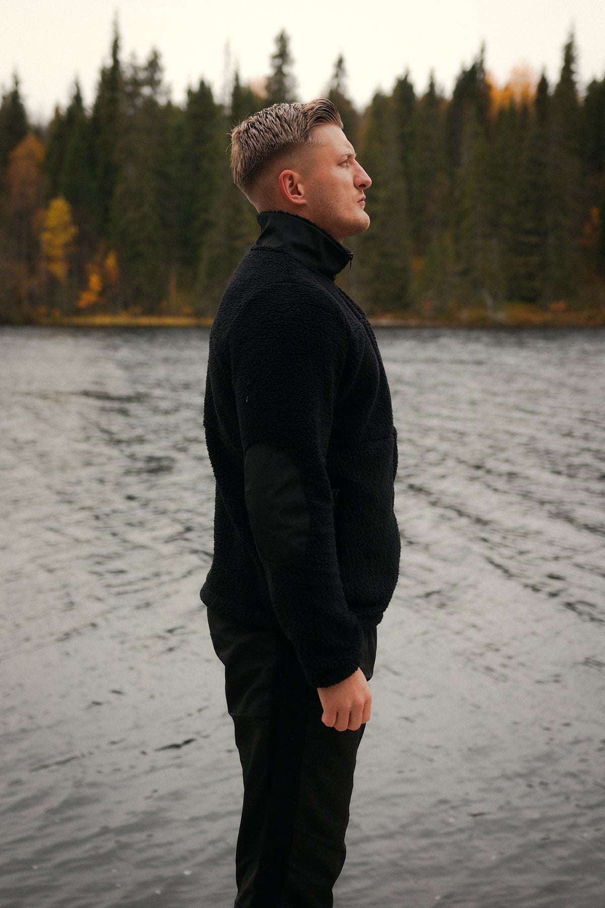Black fleece jacket with high smooth collar and textured body worn by lake
