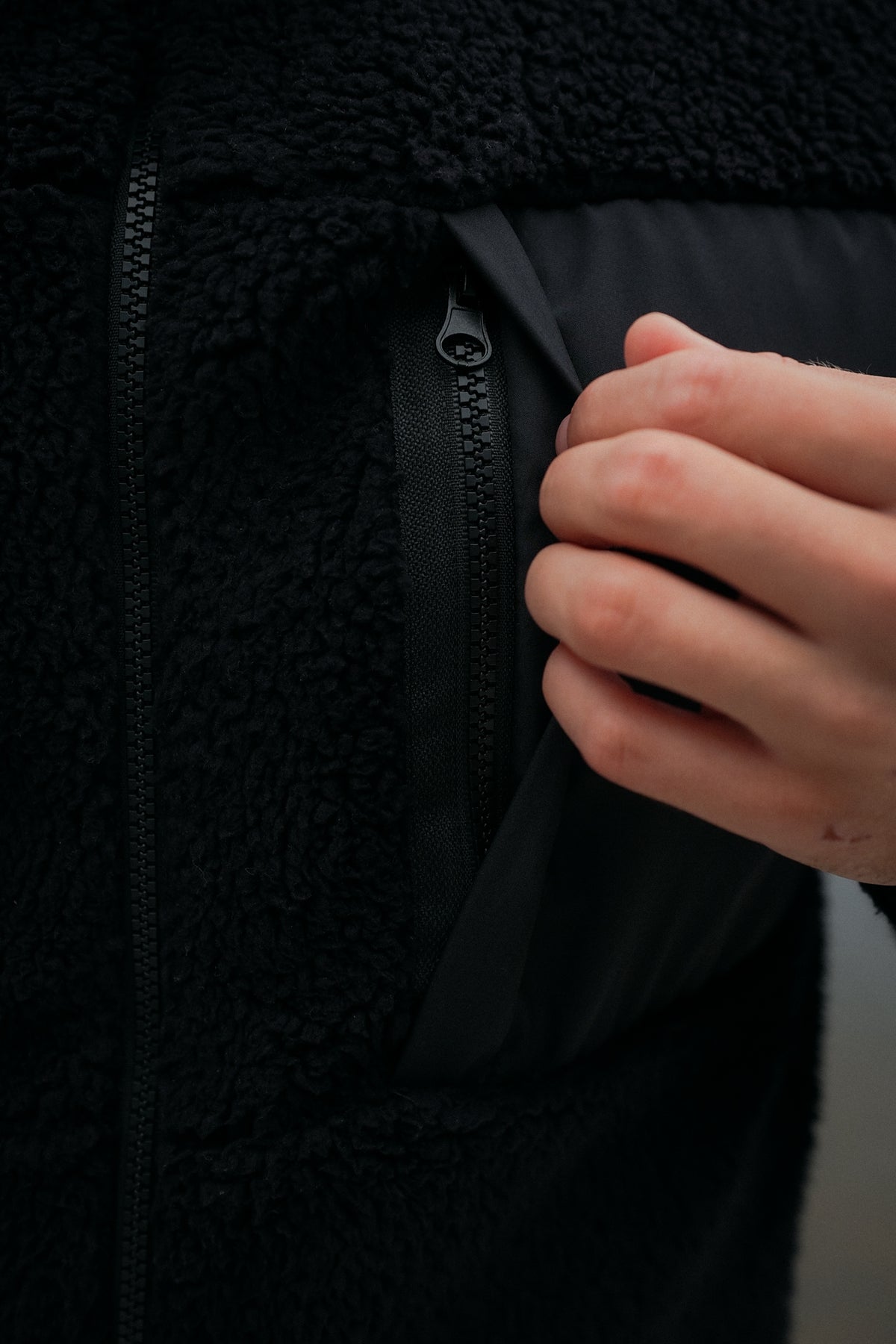 Hand opening vertical zippered pocket on black textured teddy fleece jacket