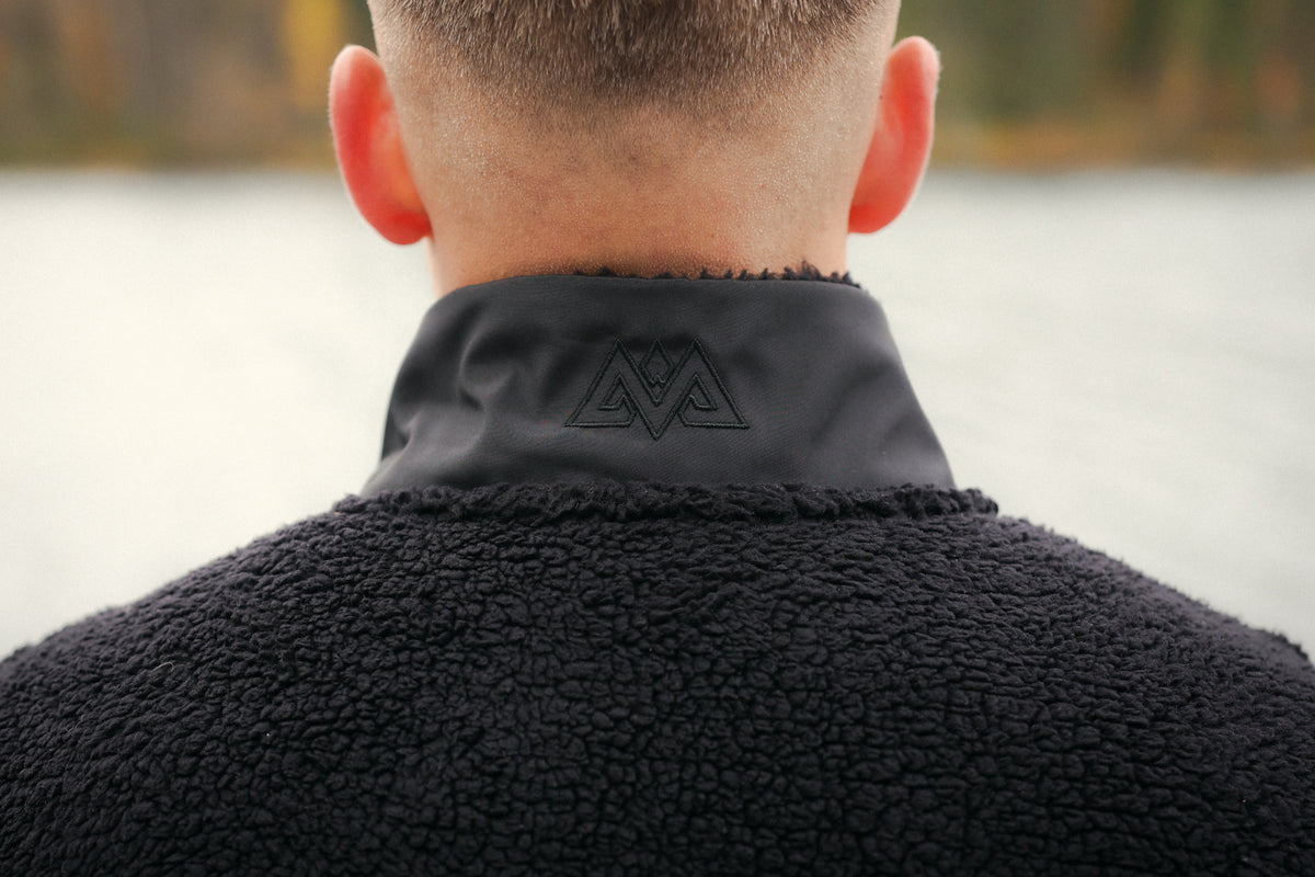 Back neck detail of black fleece jacket showing embroidered geometric logo