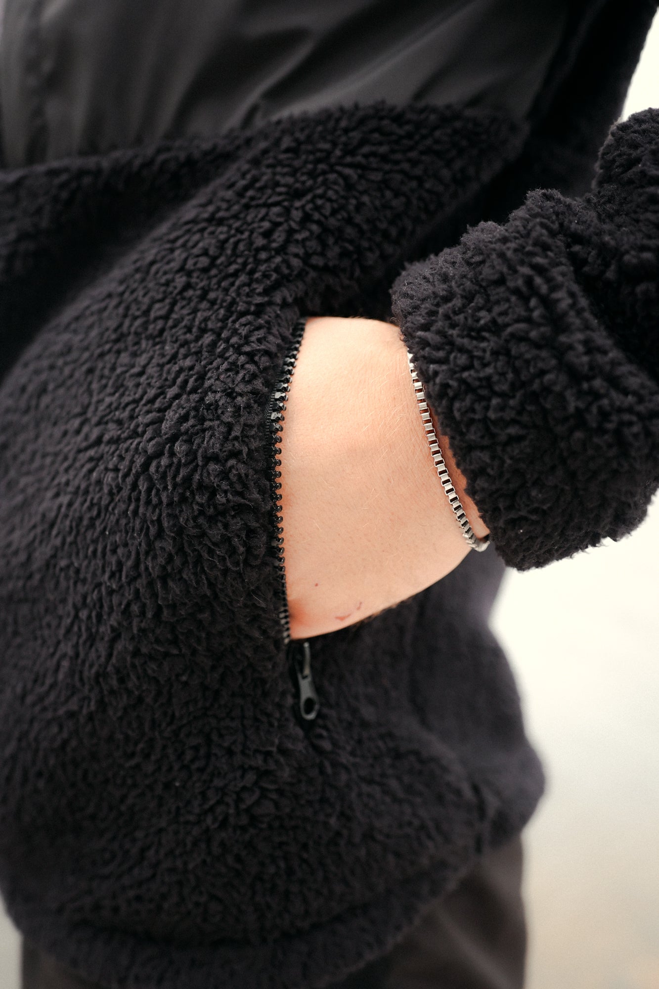 Close-up of black fleece jacket side pocket with silver zipper and fluffy texture