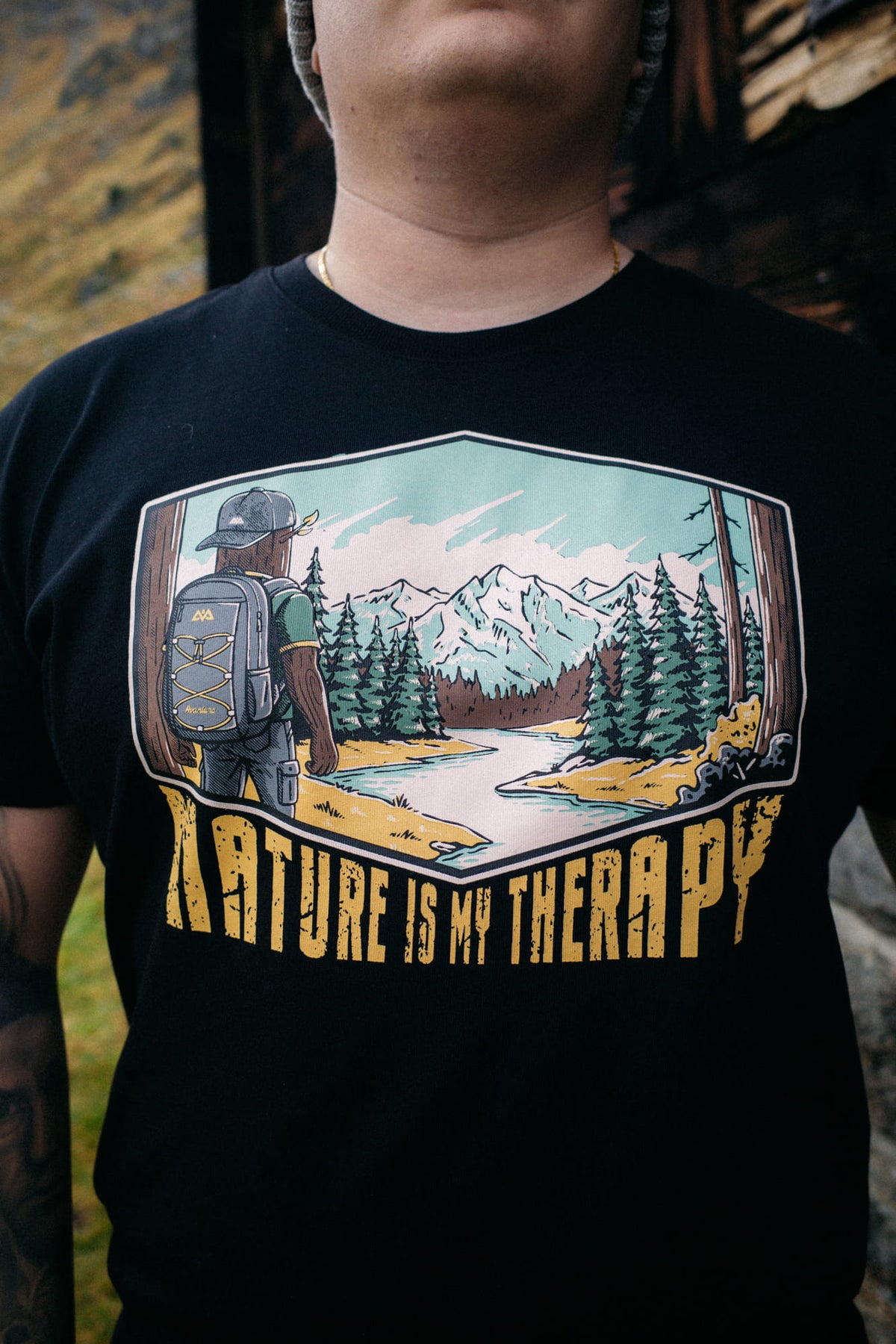 Mann trägt schwarzes Avantura T-Shirt mit Bergmotiv vor Holzinterieur