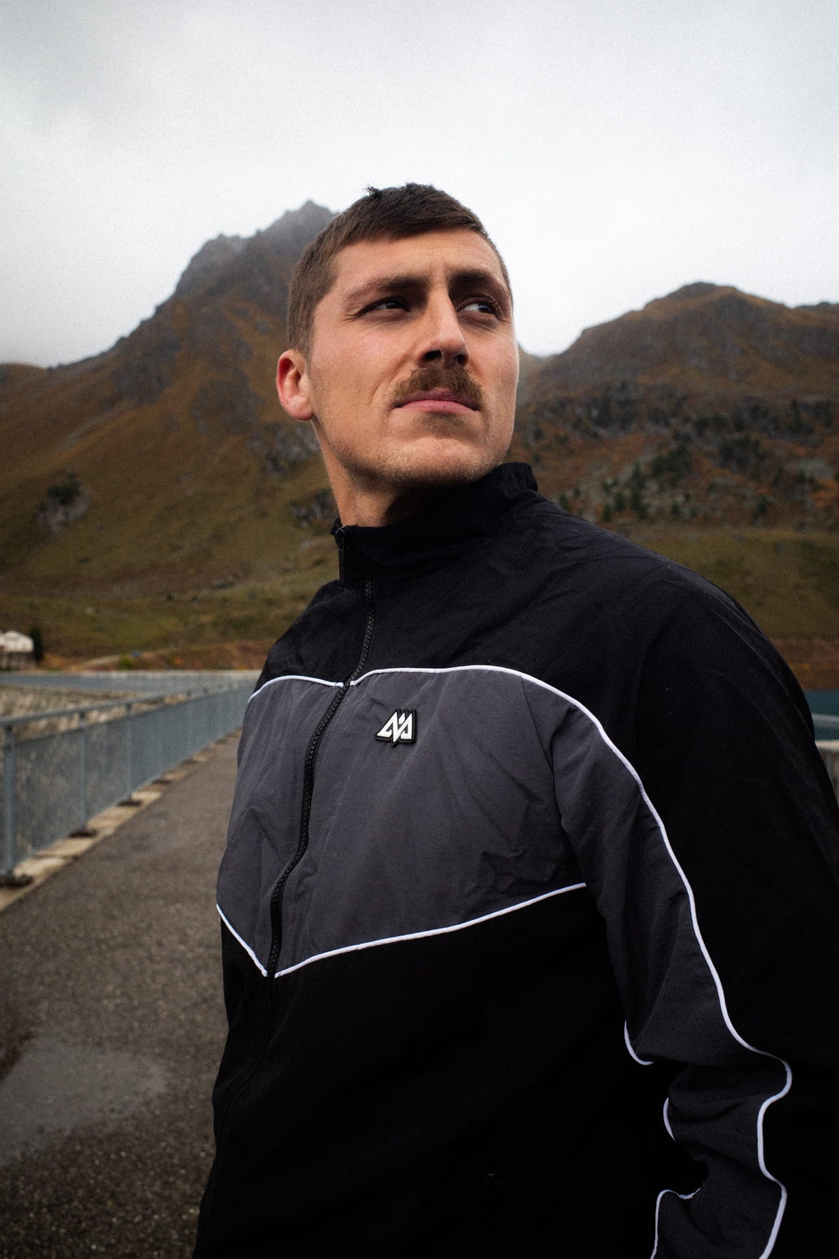 Nahaufnahme des Rubber-Logos und der Kragenstruktur der schwarz-grauen Trackjacke
