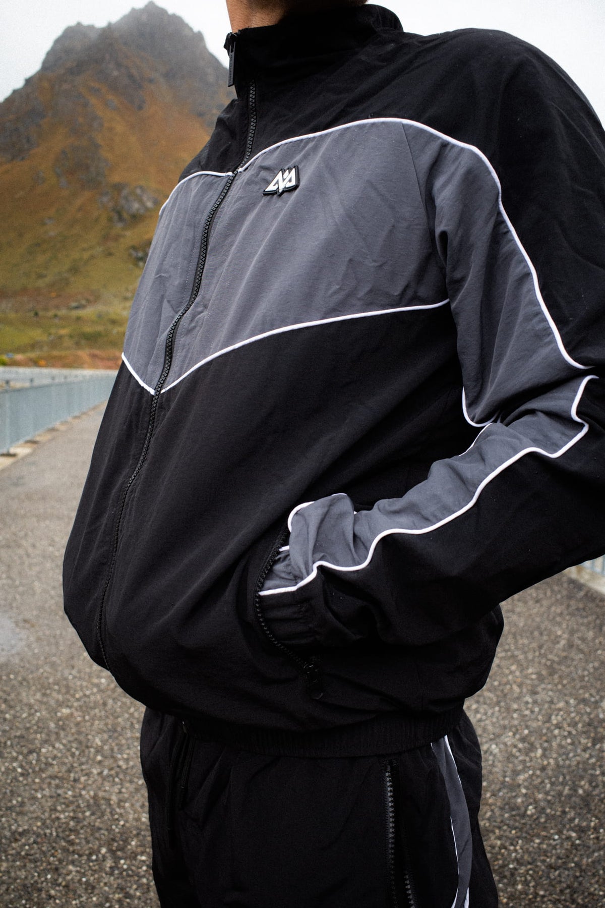 Detailaufnahme der seitlichen Reißverschlusstasche der schwarz-grauen Trackjacke