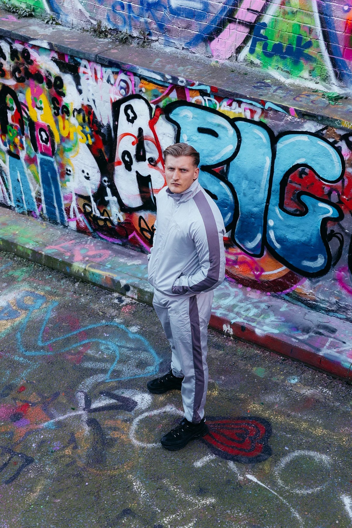 Grauer Trainingsanzug mit Seitenstreifen vor Graffiti-Wand