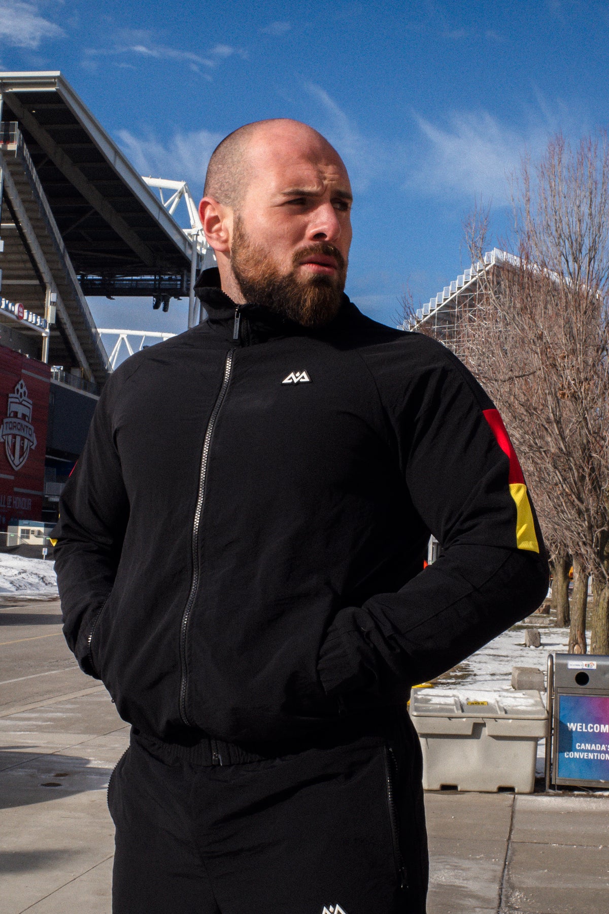 Schwarzer Trainingsanzug mit rot-goldenen Ärmelstreifen, Stadion-Hintergrund