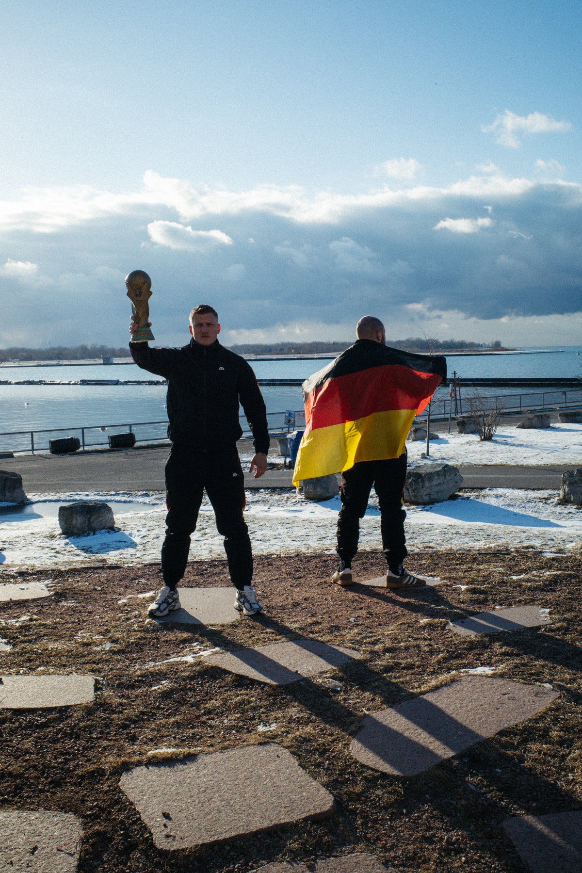 Zwei Männer in schwarzen Avantura Tracksuits mit deutscher Flagge und Trophäe