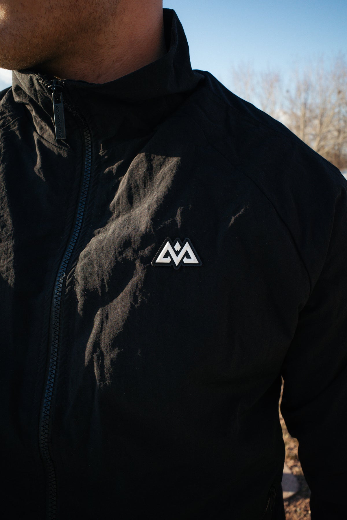 Detailaufnahme schwarze Jacke mit Reißverschluss und dreieckigem Rubber-Logo