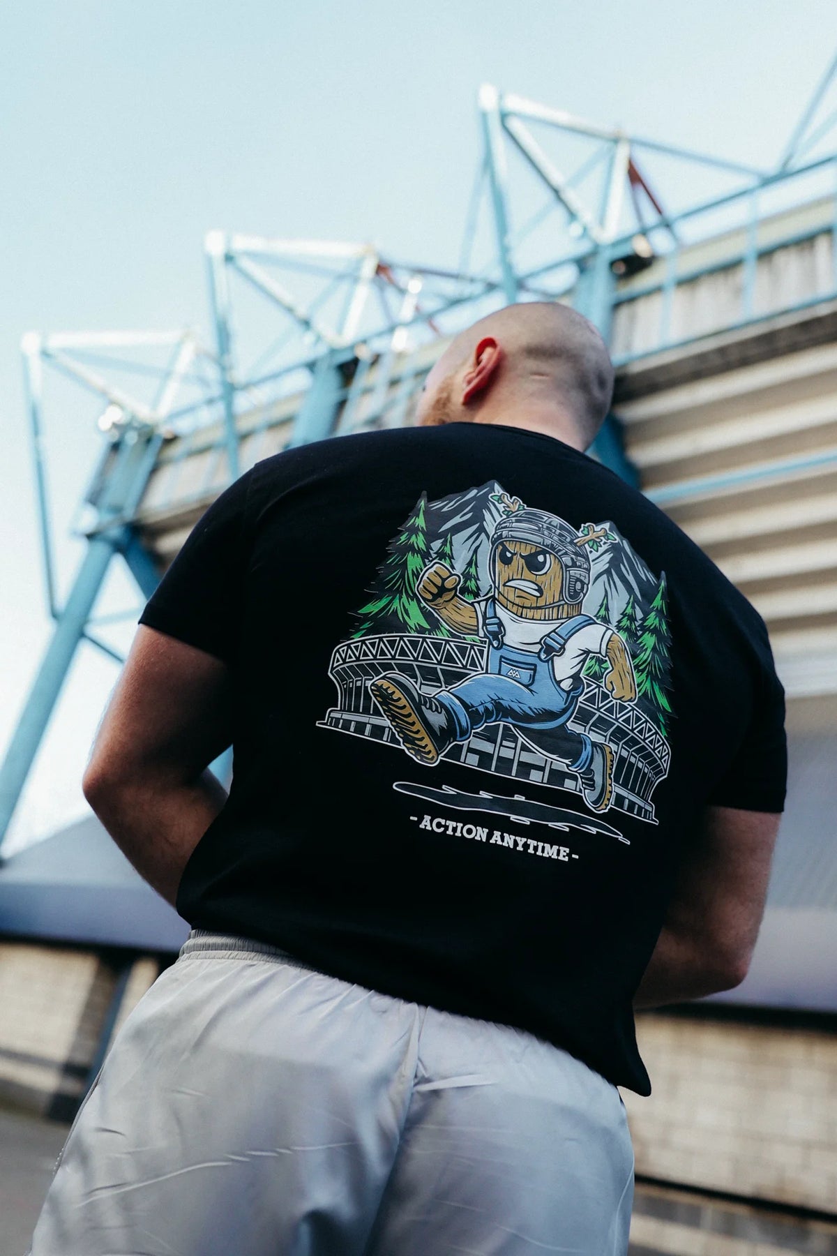 Low angle rear shot of black T-shirt showing tree trunk mascot leaping over bridge graphic