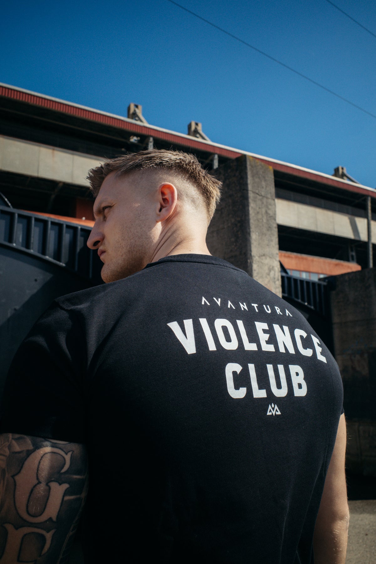 Black T-shirt with white print in front of industrial architecture