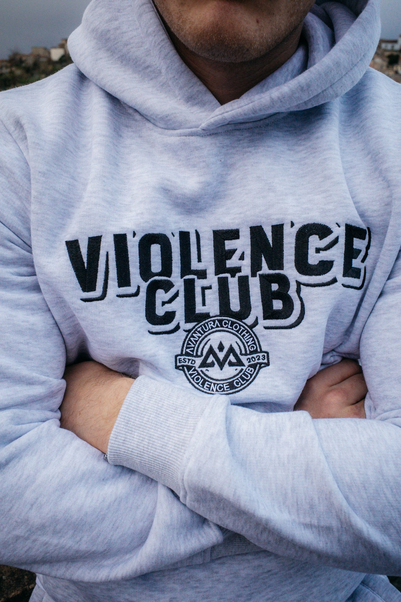 Detail of black embroidered VIOLENCE CLUB text and circular logo on grey hoodie