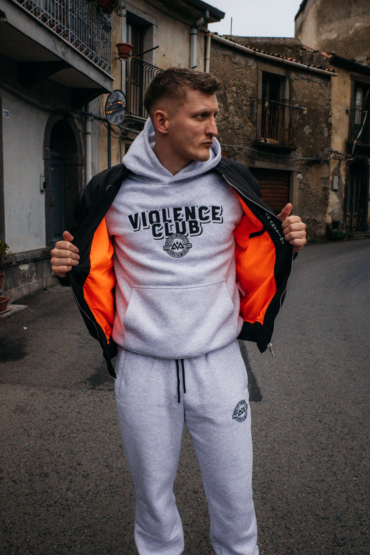Grauer VIOLENCE CLUB Hoodie unter offener schwarzer Jacke mit orangefarbenem Futter