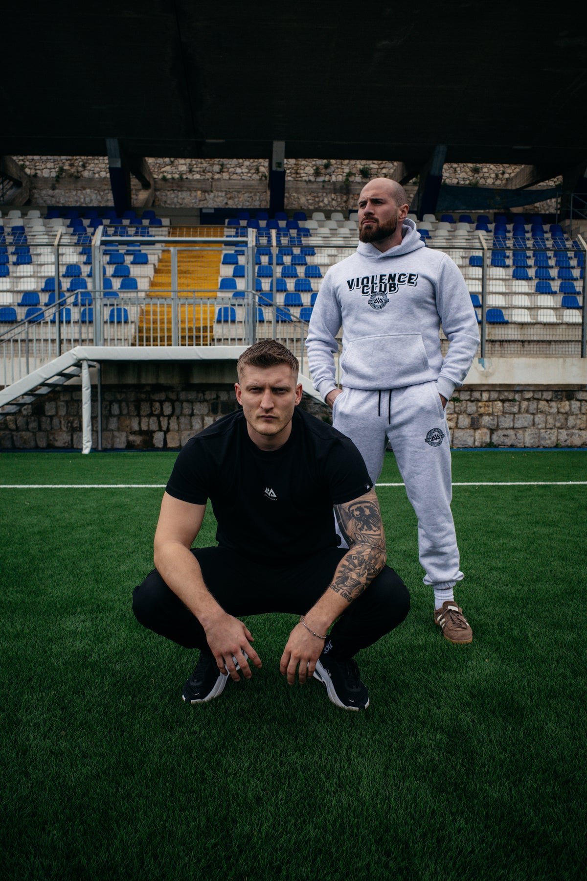 Two men posing in stadium seats wearing light grey heathered sweat suit sets