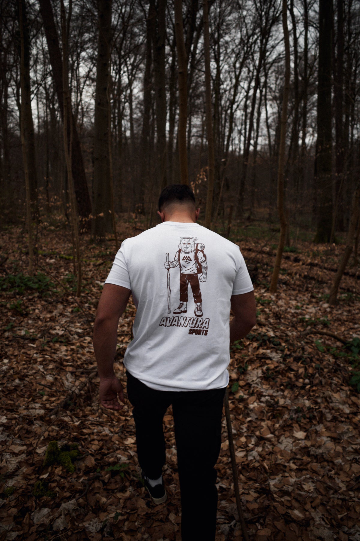 Man wearing white Avantura T-shirt with large brown hiking character back design