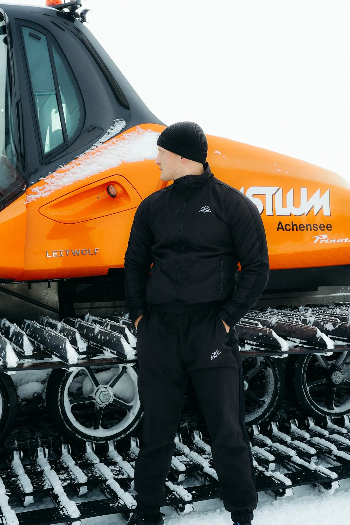 Men's black full-zip tracksuit set worn in snowy mountain setting
