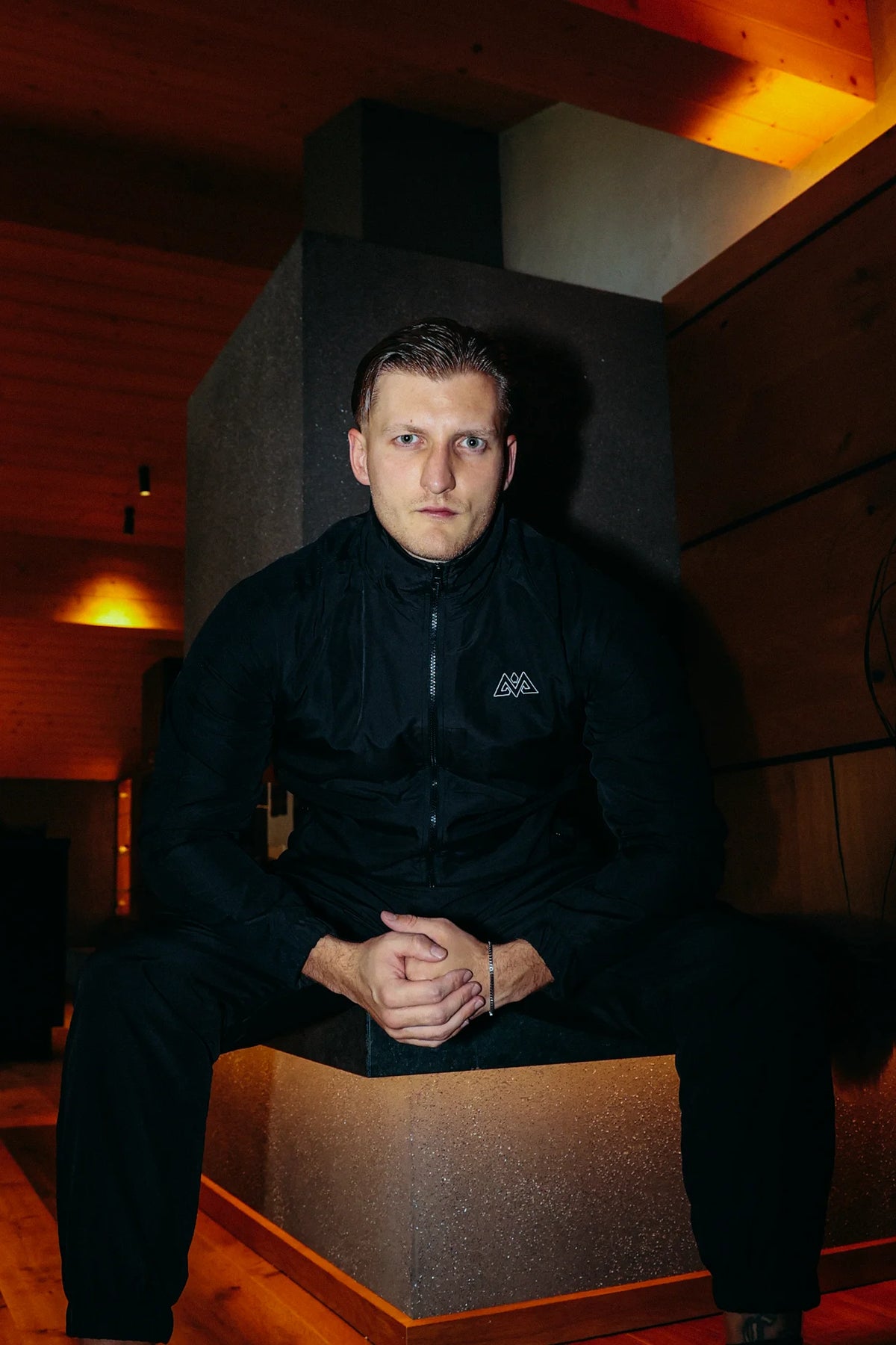 Full black tracksuit with white chest logo in modern indoor setting