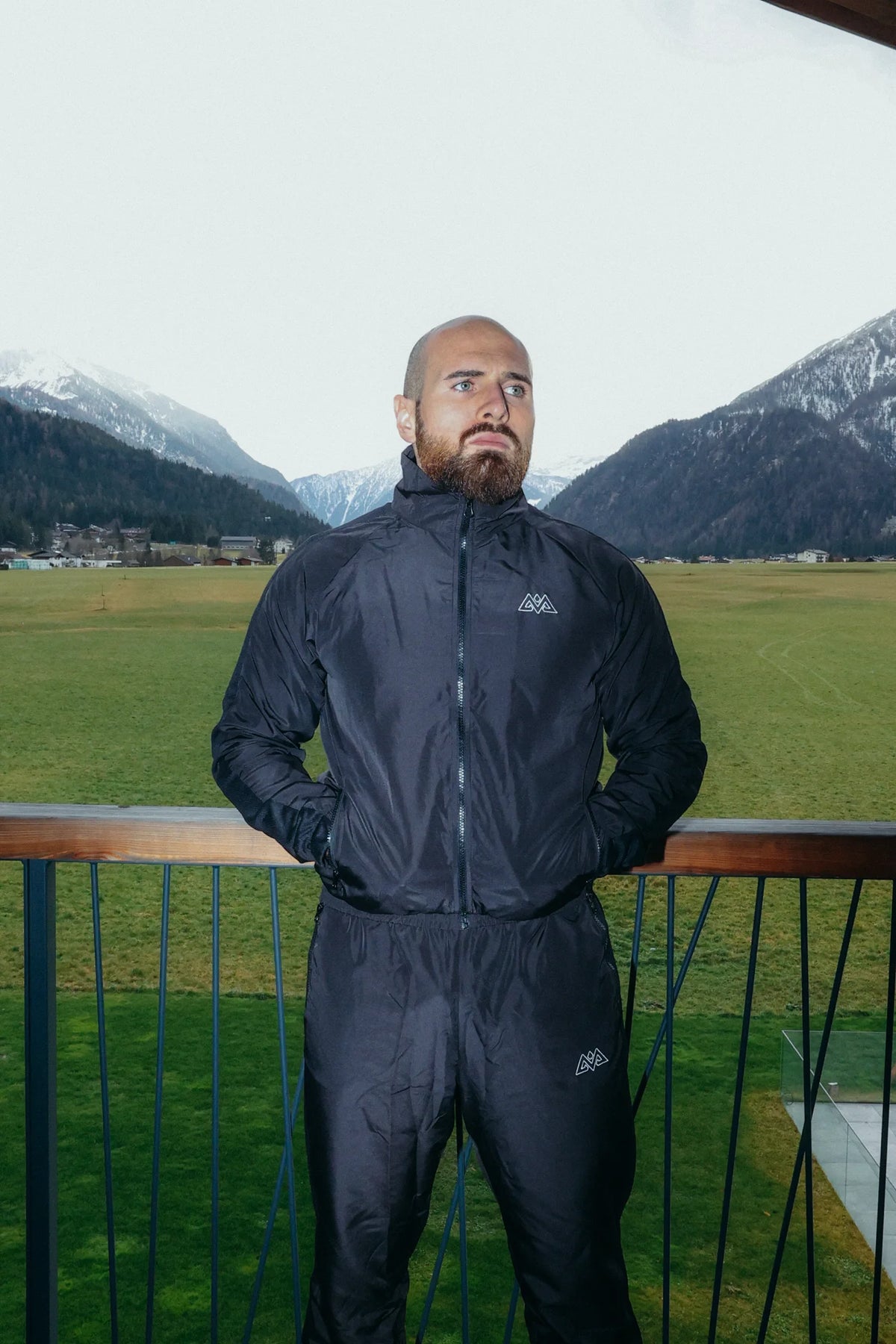 Man wearing black zip-up tracksuit on balcony overlooking mountains