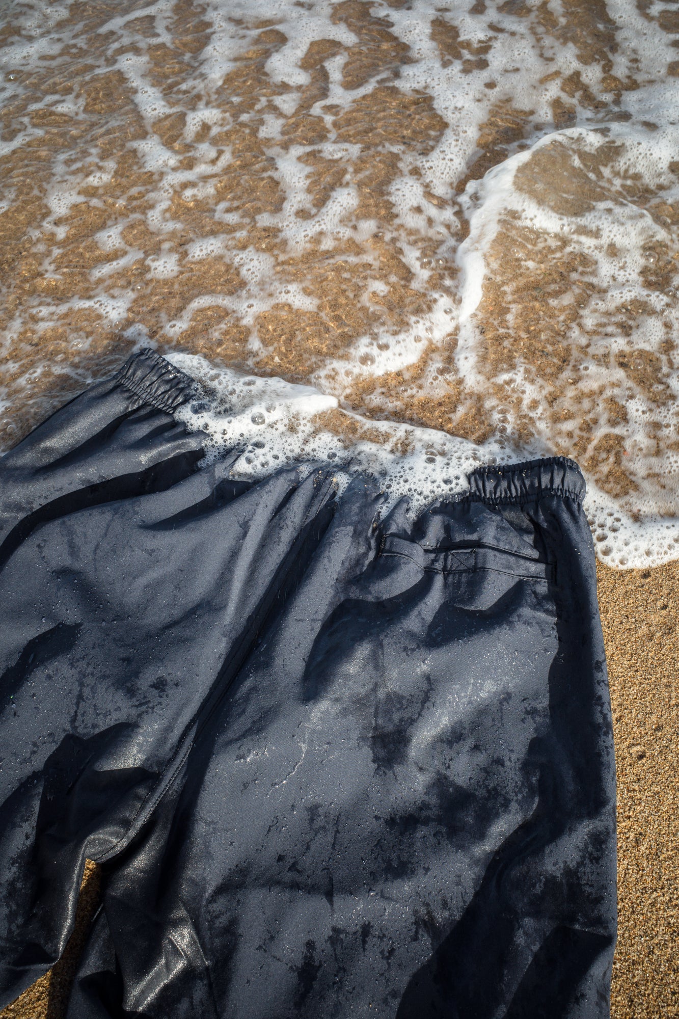 Wet navy swim trunks flat lay on beach sand