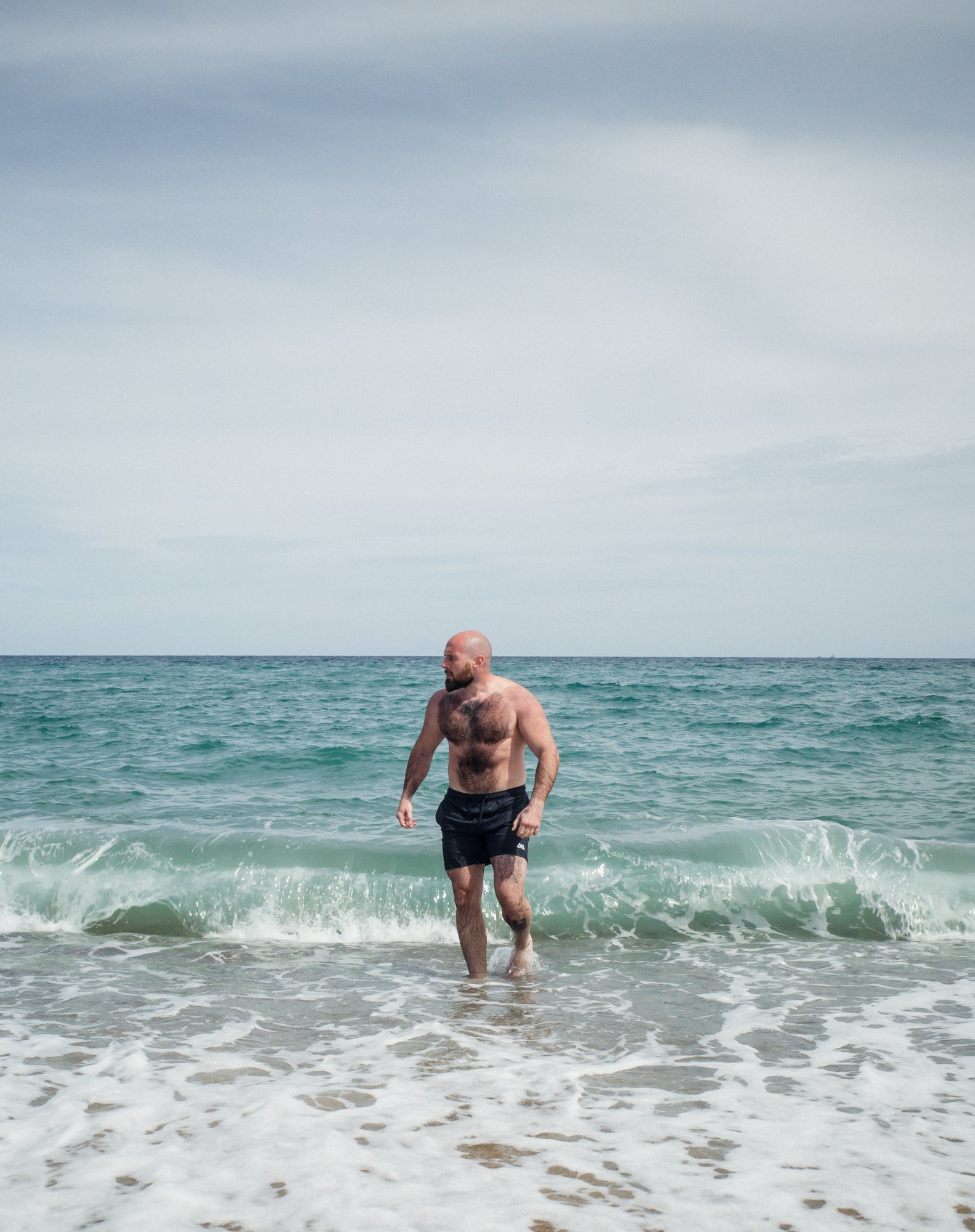 Man walking out of ocean in navy swim trunks