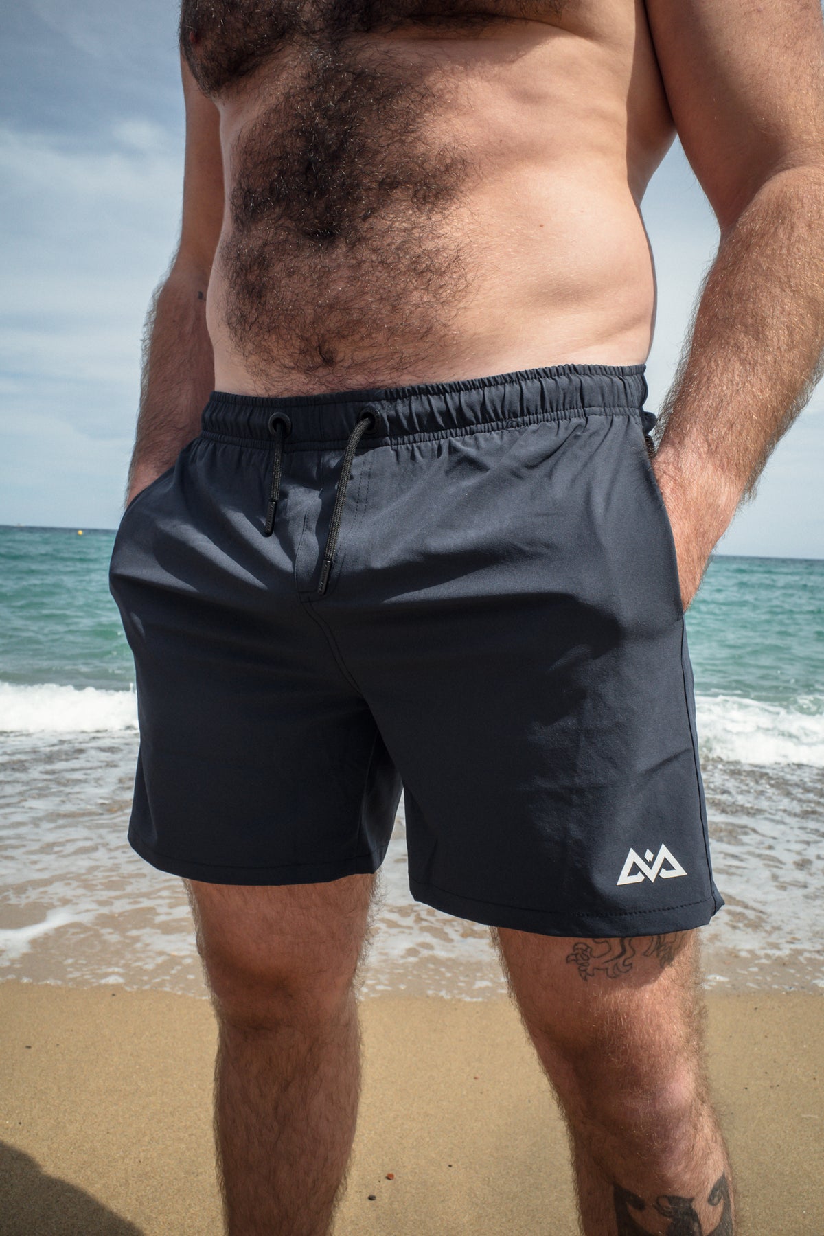 Front view of man in navy swim trunks with hands in pockets