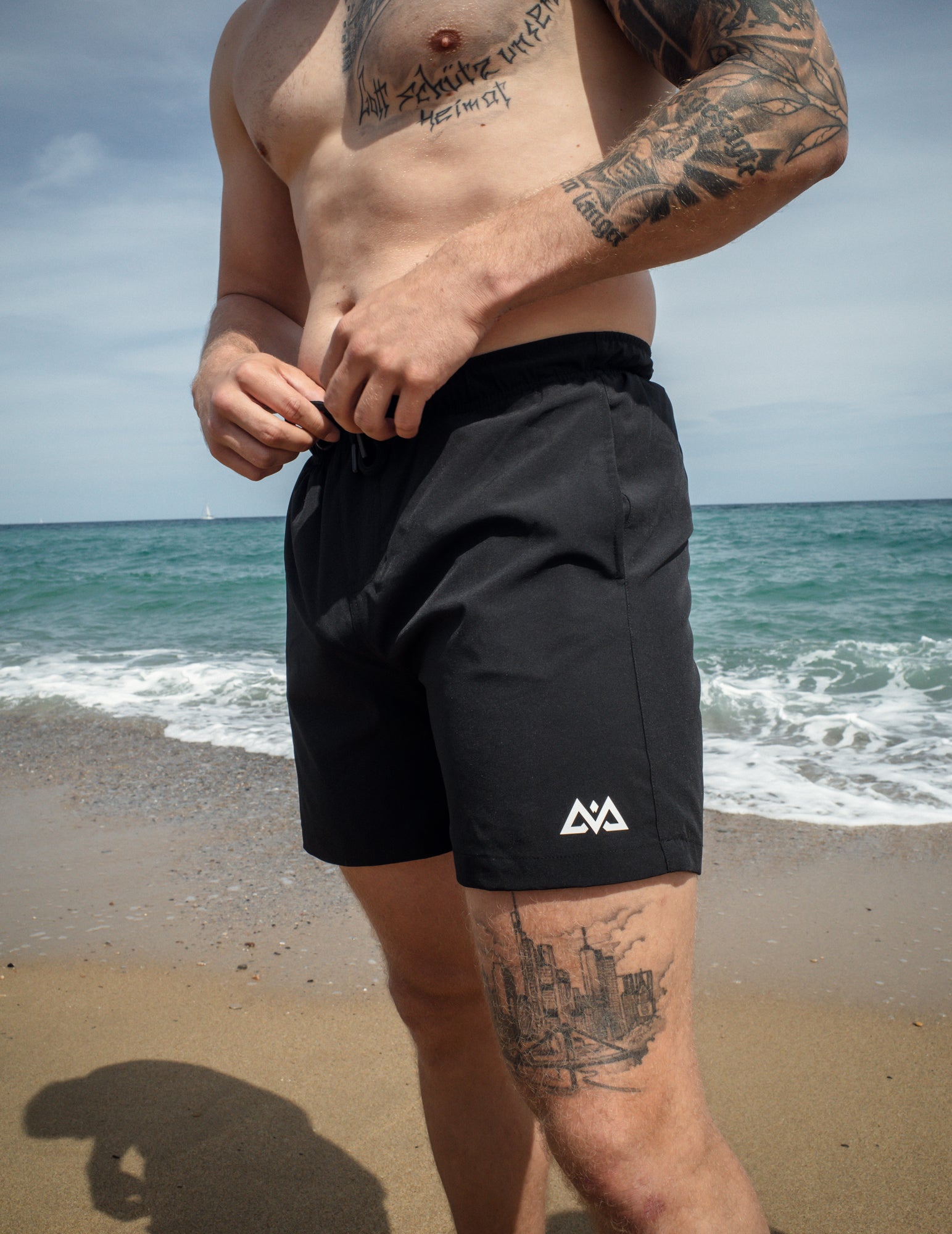 Man adjusting black AVA logo swim shorts on beach