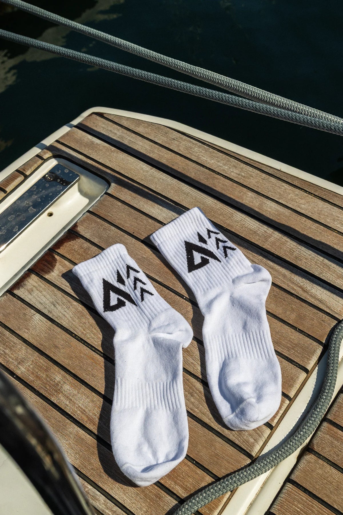 Close-up of white ribbed crew socks with woven black logo laid flat on wooden deck