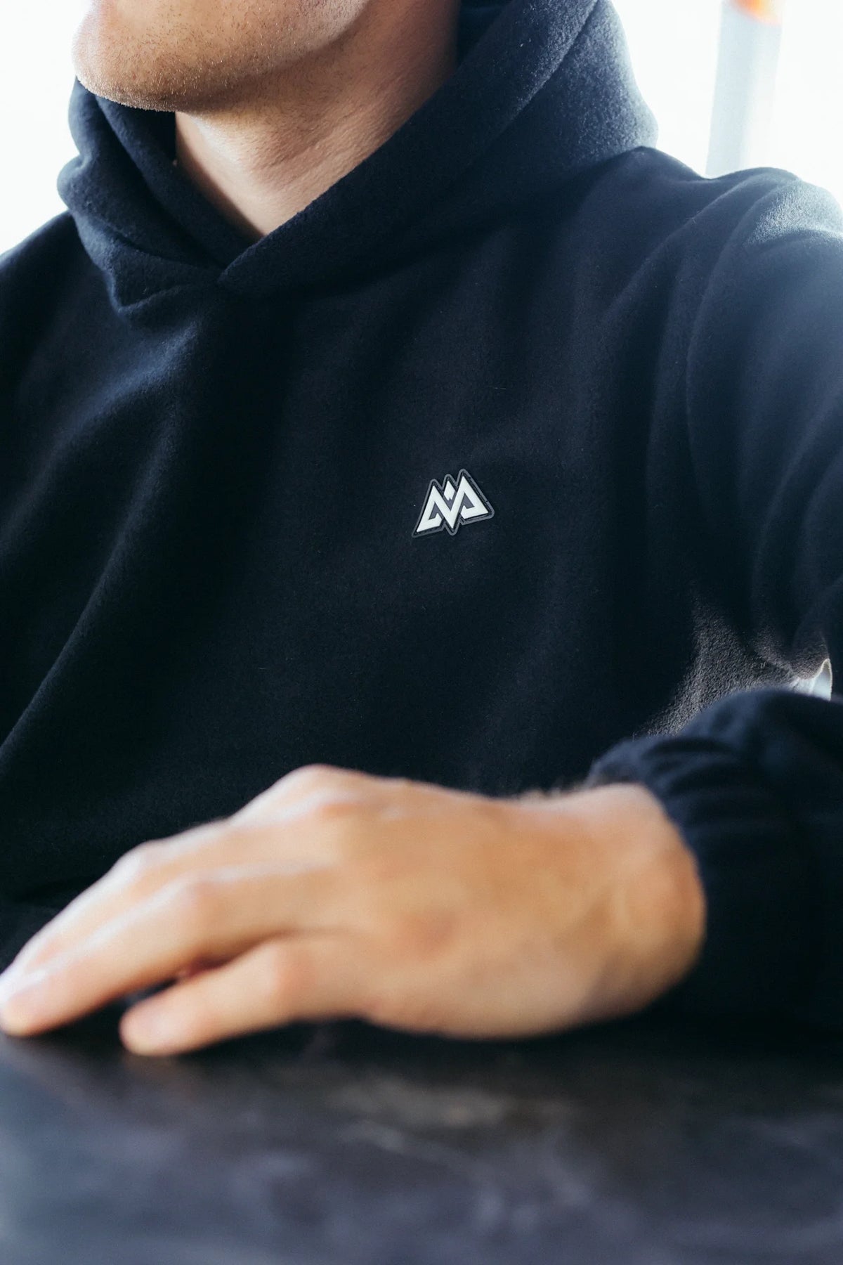 Close-up of white embroidered mountain logo on black fleece hoodie fabric texture