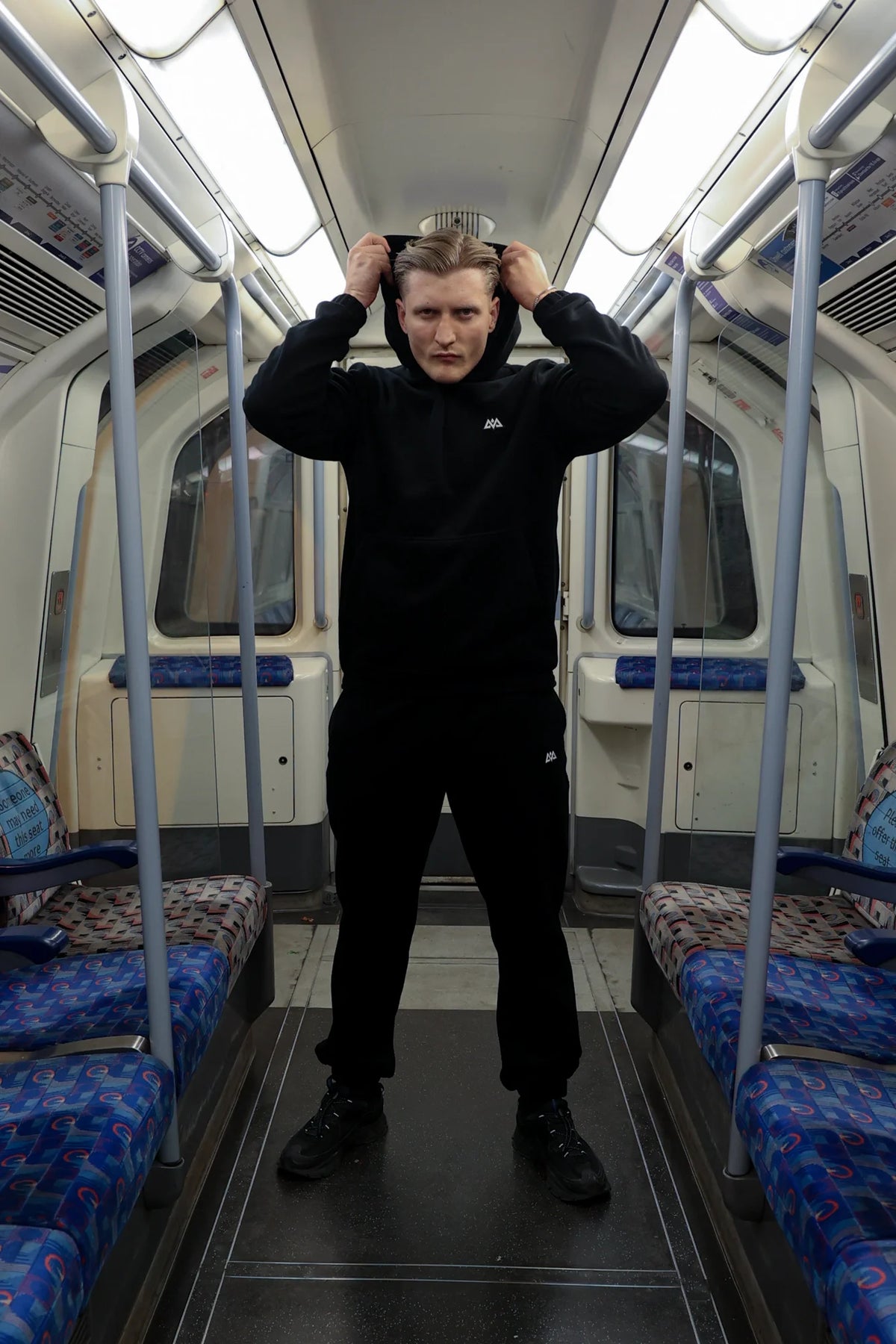 Adjusting hood of black AVA Logo Fleece Hoodie with matching sweatpants in transit