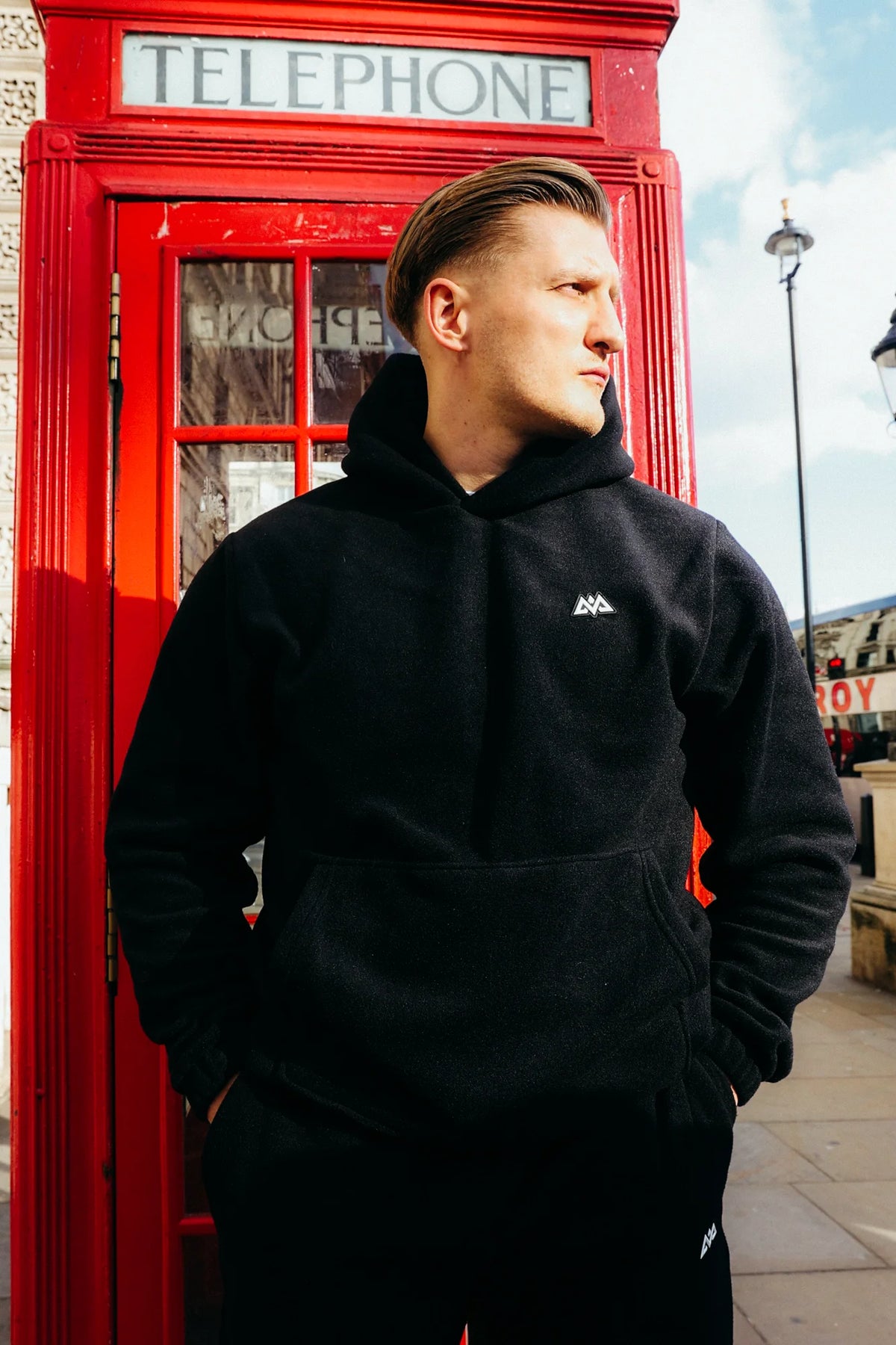Black AVA Logo Fleece Hoodie with geometric chest logo worn by man in urban setting