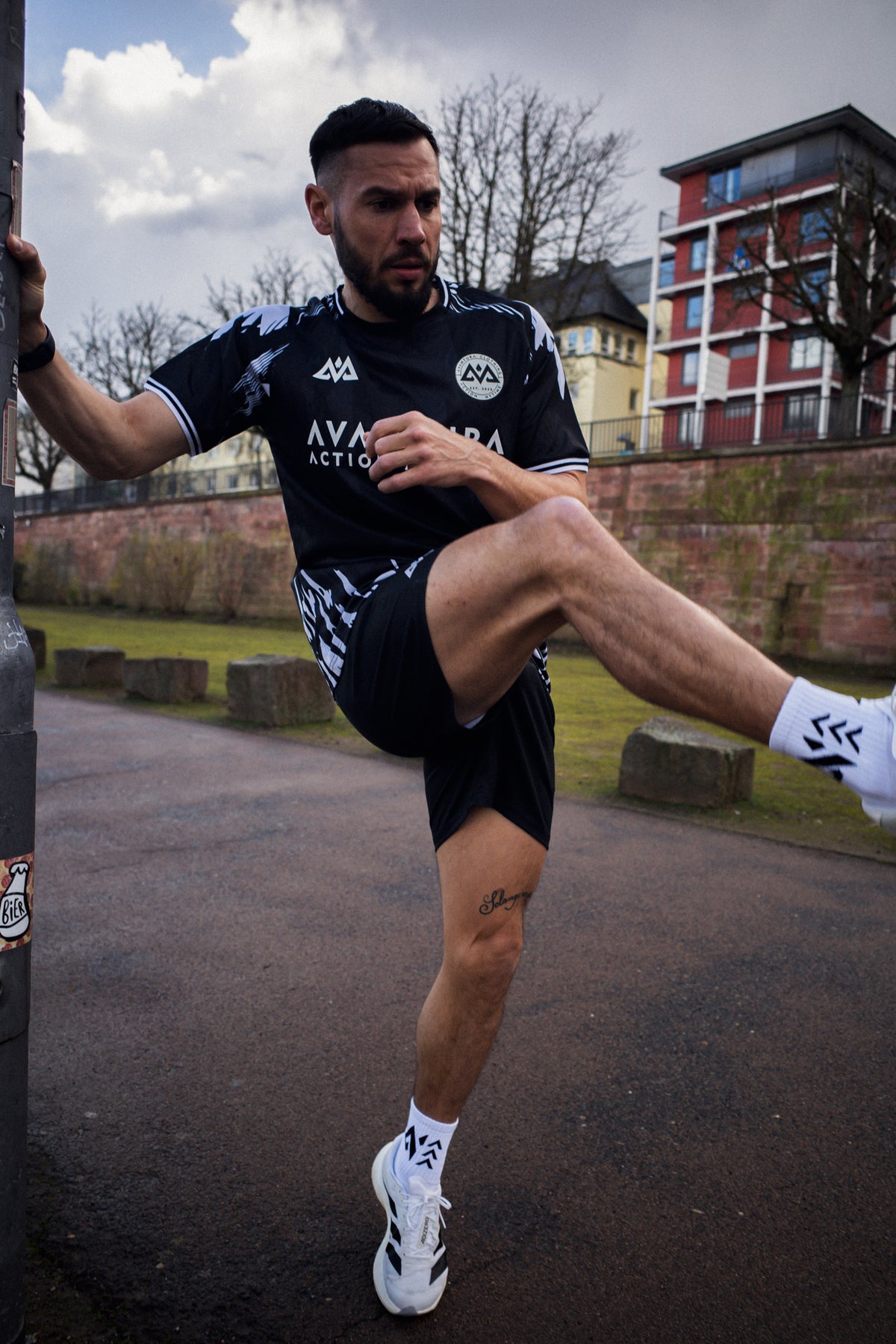 Man stretching in black athletic jersey with circular chest logo